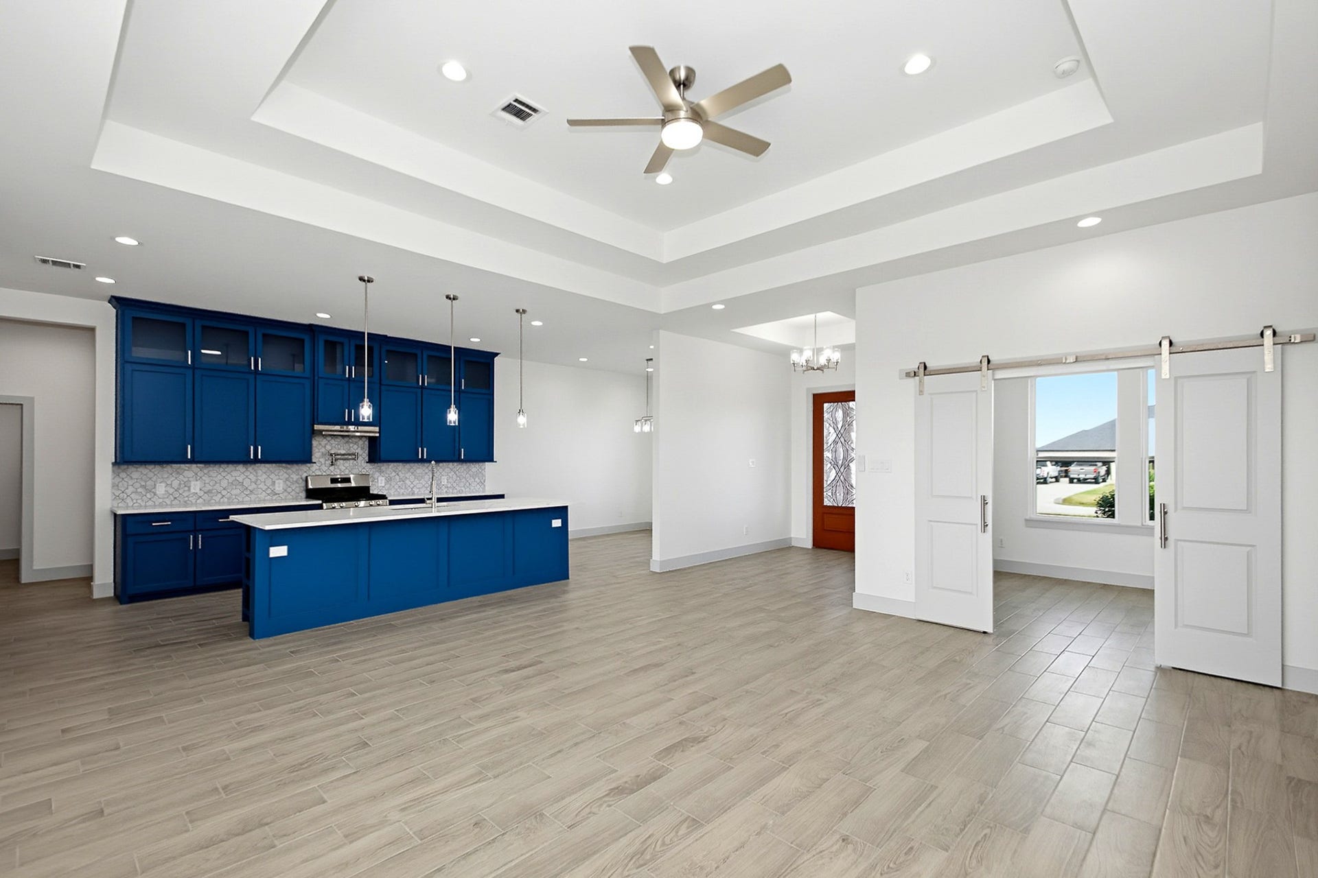 619 Longhorn Trail, Angleton, TX 77515 Spacious 19x16 open-concept living area featuring a modern kitchen with striking blue cabinetry, elegant pendant lighting, and a large center island, complemented by sleek flooring and stylish barn doors.