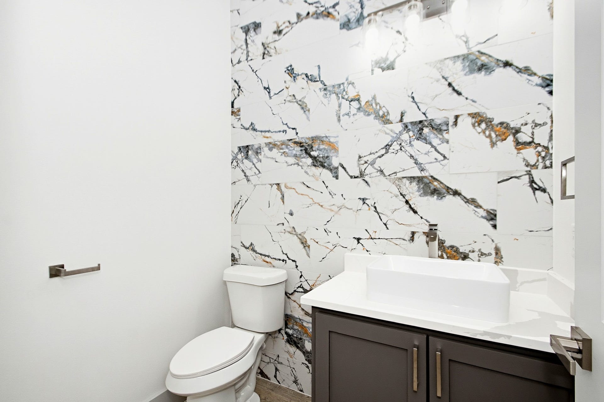 619 Longhorn Trail, Angleton, TX 77515 Elegant half bathroom featuring a striking marble-patterned accent wall, modern vanity, and sleek fixtures for a sophisticated touch.