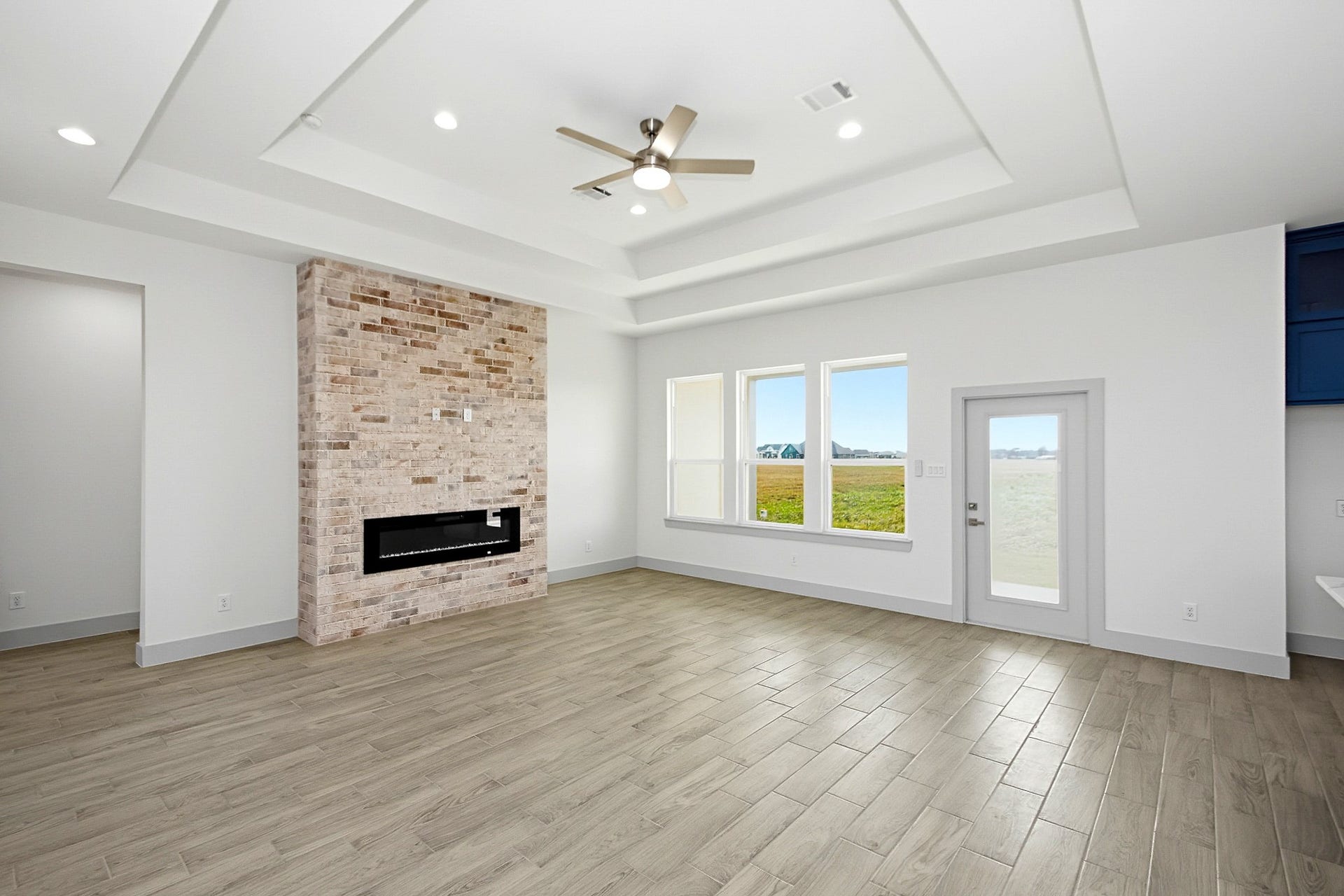 619 Longhorn Trail, Angleton, TX 77515 Spacious 19x16 living area with elegant tray ceiling, modern recessed lighting, and a stylish brick fireplace. Large windows and a glass door offer abundant natural light and views of the surrounding landscape.