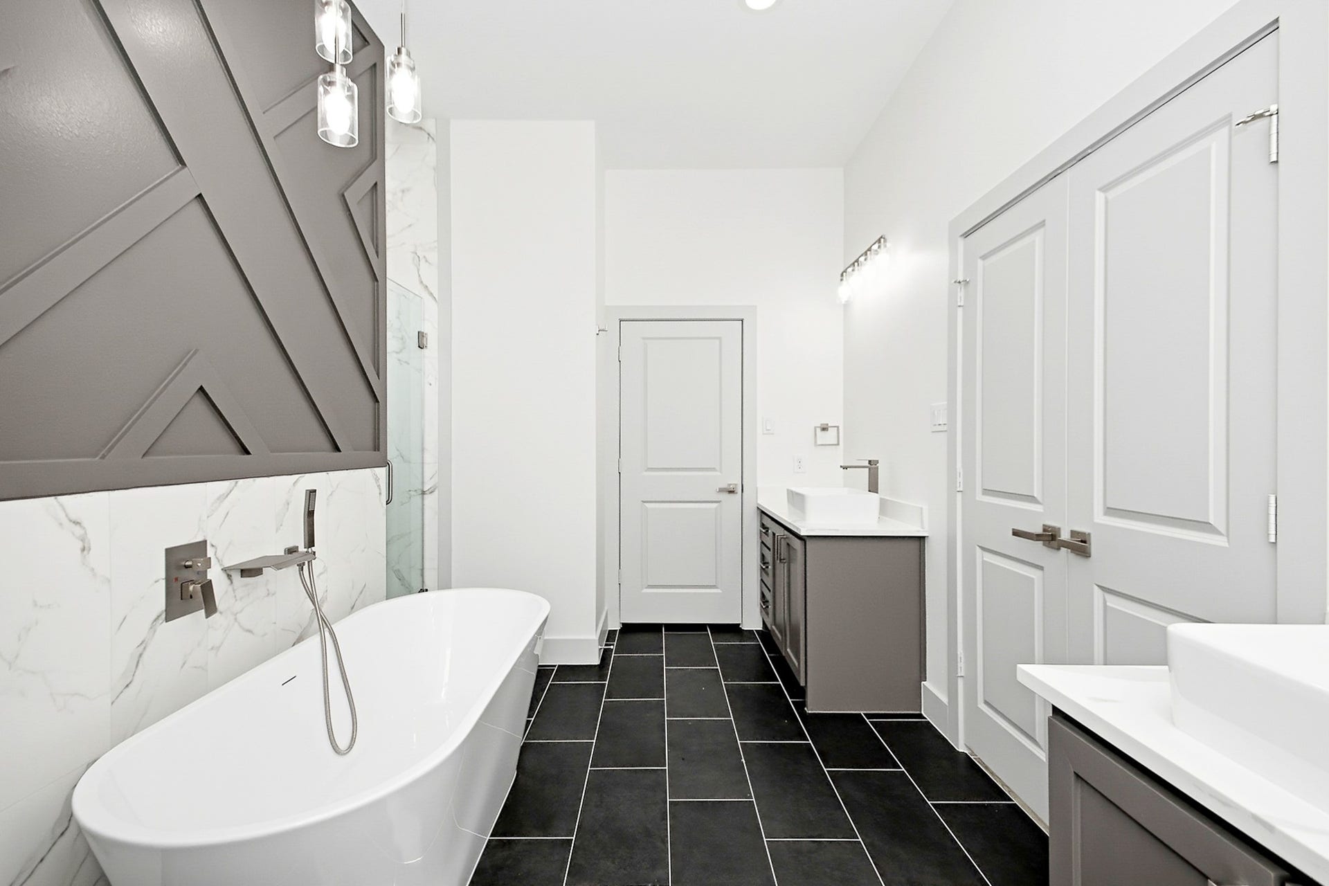 619 Longhorn Trail, Angleton, TX 77515 Luxurious primary 16x12 bathroom featuring a sleek freestanding bathtub, modern fixtures, and stylish geometric accent wall, complemented by elegant black tile flooring and dual vanities.
