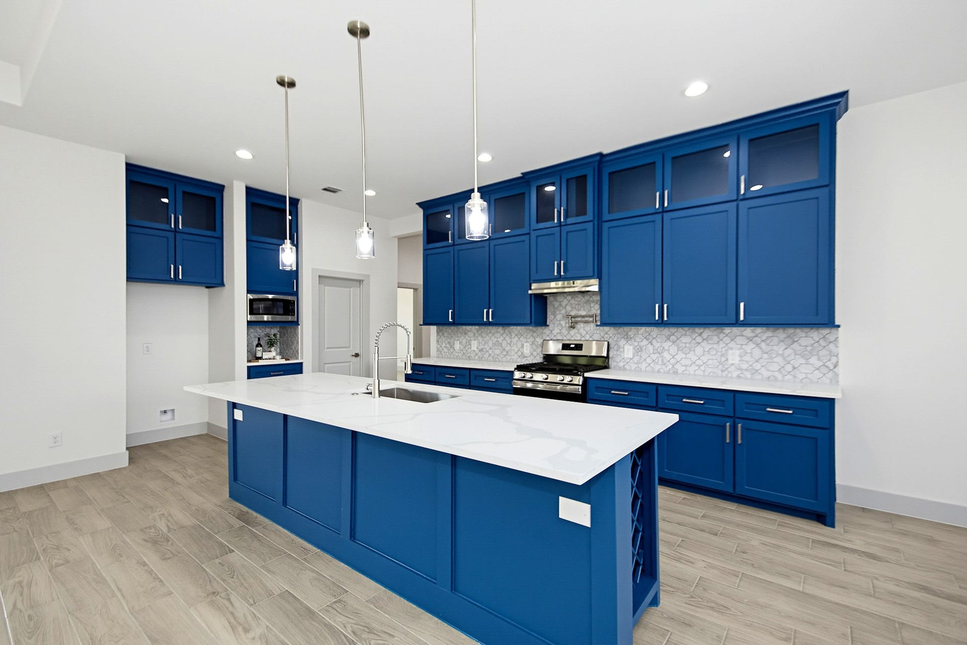 619 Longhorn Trail, Angleton, TX 77515 A modern 19x14 kitchen featuring vibrant blue cabinetry, sleek stainless-steel appliances, and elegant pendant lighting over a spacious island with a white quartz countertop.