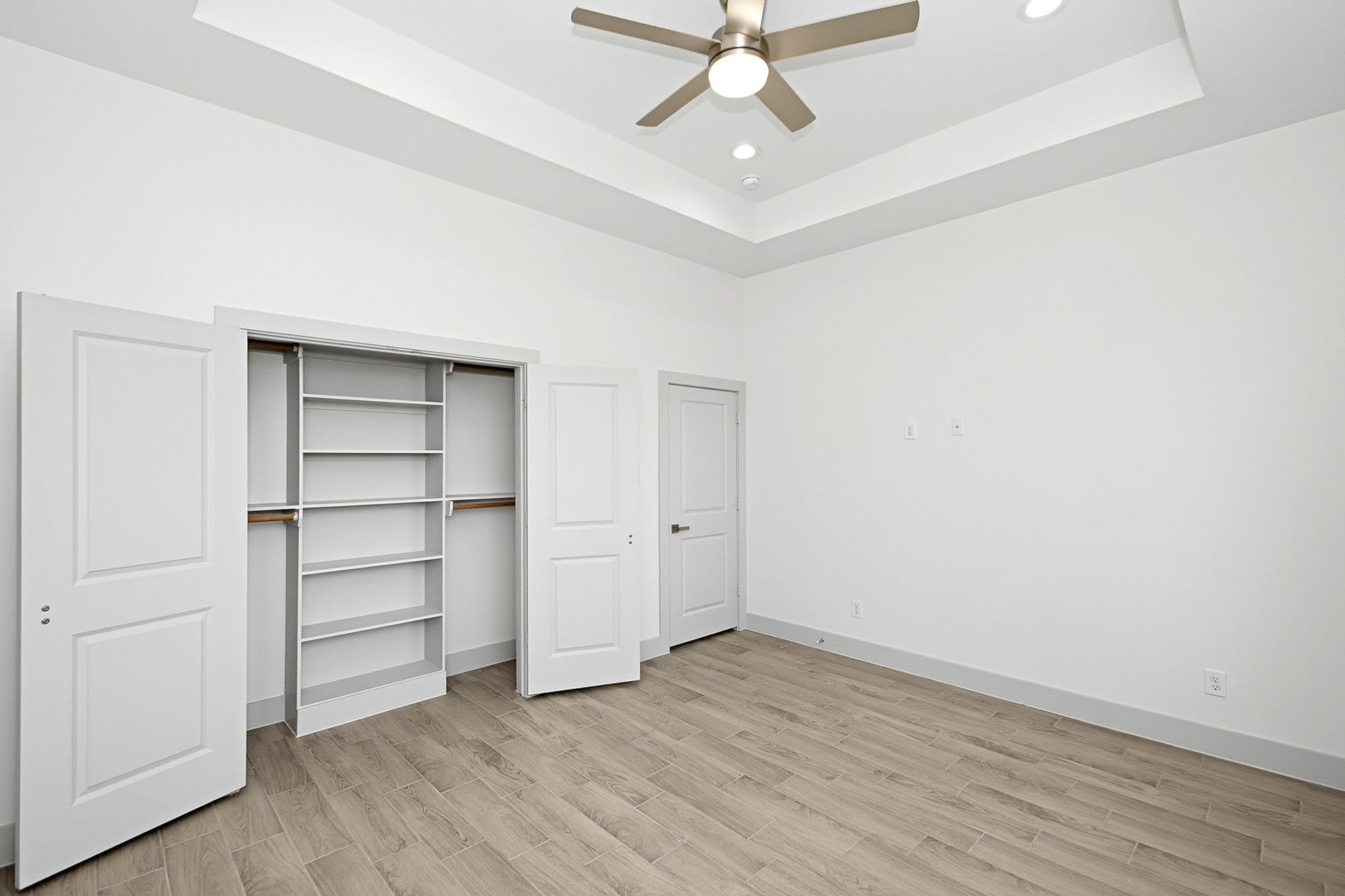 619 Longhorn Trail, Angleton, TX 77515 Spacious 14.5x12 bedroom featuring a tray ceiling, modern ceiling fan, and ample closet storage with built-in shelving.