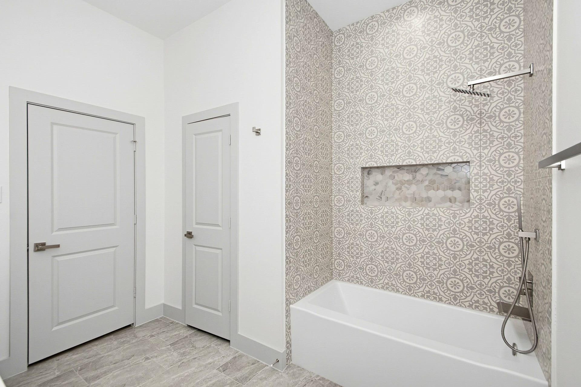 619 Longhorn Trail, Angleton, TX 77515 Elegant 10x10 secondary bathroom featuring a stylish patterned tile wall, modern fixtures, and a sleek bathtub with built-in shelving.