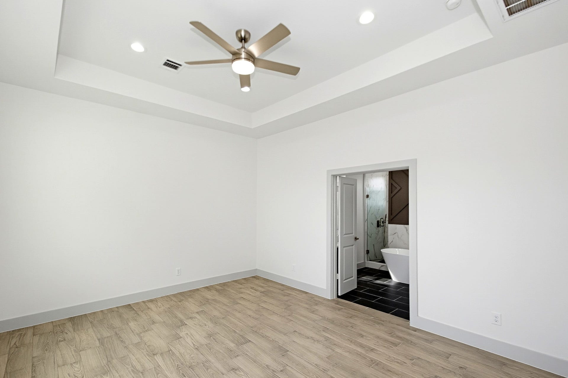 619 Longhorn Trail, Angleton, TX 77515 Spacious 16x13 Primary bedroom with elegant tile flooring, a modern ceiling fan, and recessed lighting, leading to a luxurious bathroom with a freestanding tub.