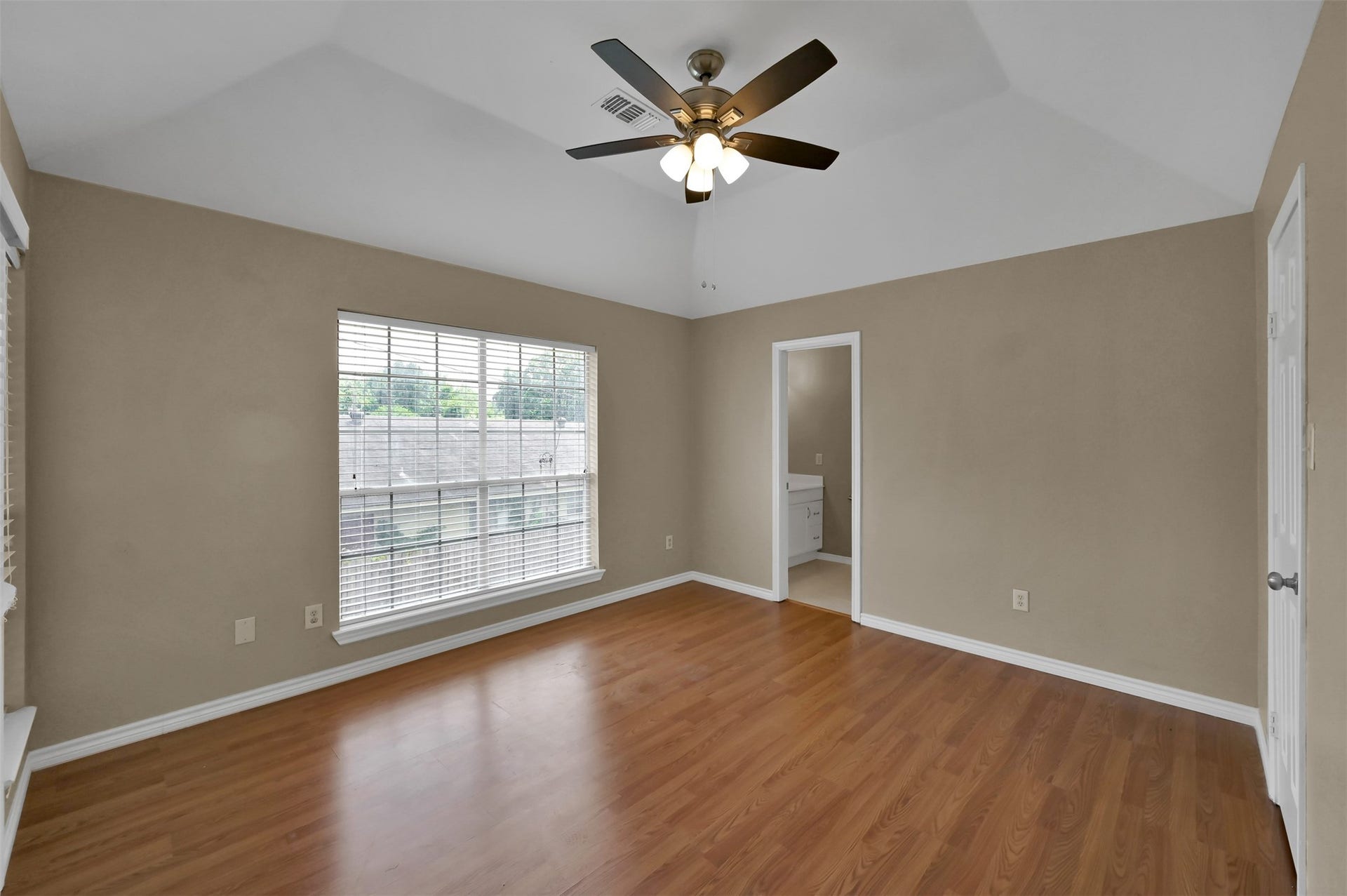 1141 Lovett Street, Tomball, TX 77375 Spacious bedroom with warm wood flooring, abundant natural light from a large window, and a ceiling fan for comfort.