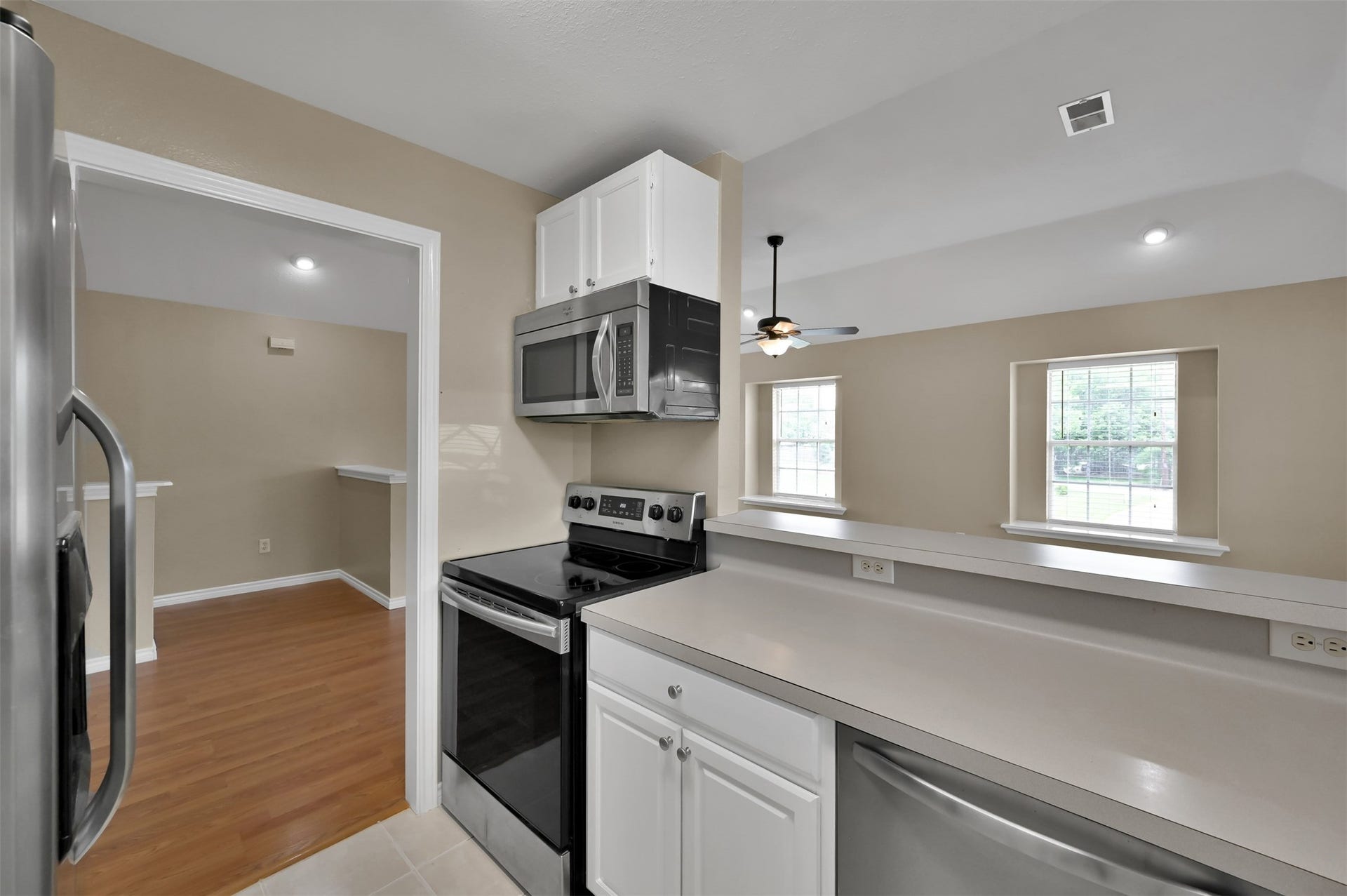 1141 Lovett Street, Tomball, TX 77375 Modern kitchen with stainless steel appliances, sleek countertops, and a view into a bright living area featuring large windows and a ceiling fan.