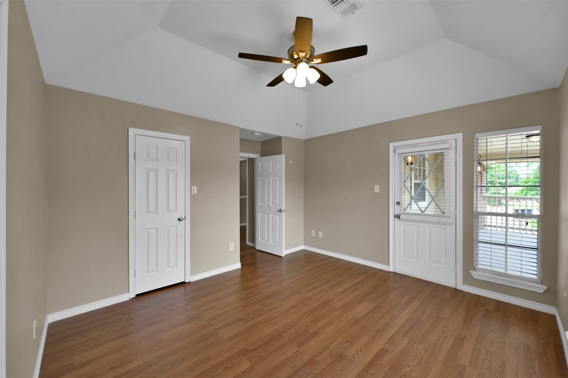 1141 Lovett Street, Tomball, TX 77375 Spacious room with vaulted ceiling, warm wood flooring, and ample natural light from large windows, complemented by a ceiling fan for comfort.