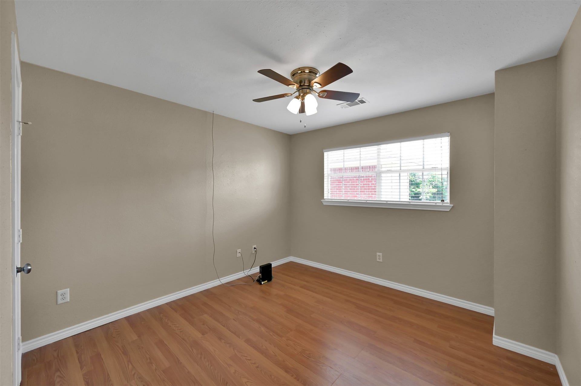 1141 Lovett Street, Tomball, TX 77375 Second bedroom with warm wood laminate flooring, neutral walls, and a ceiling fan, featuring a bright window for natural light.