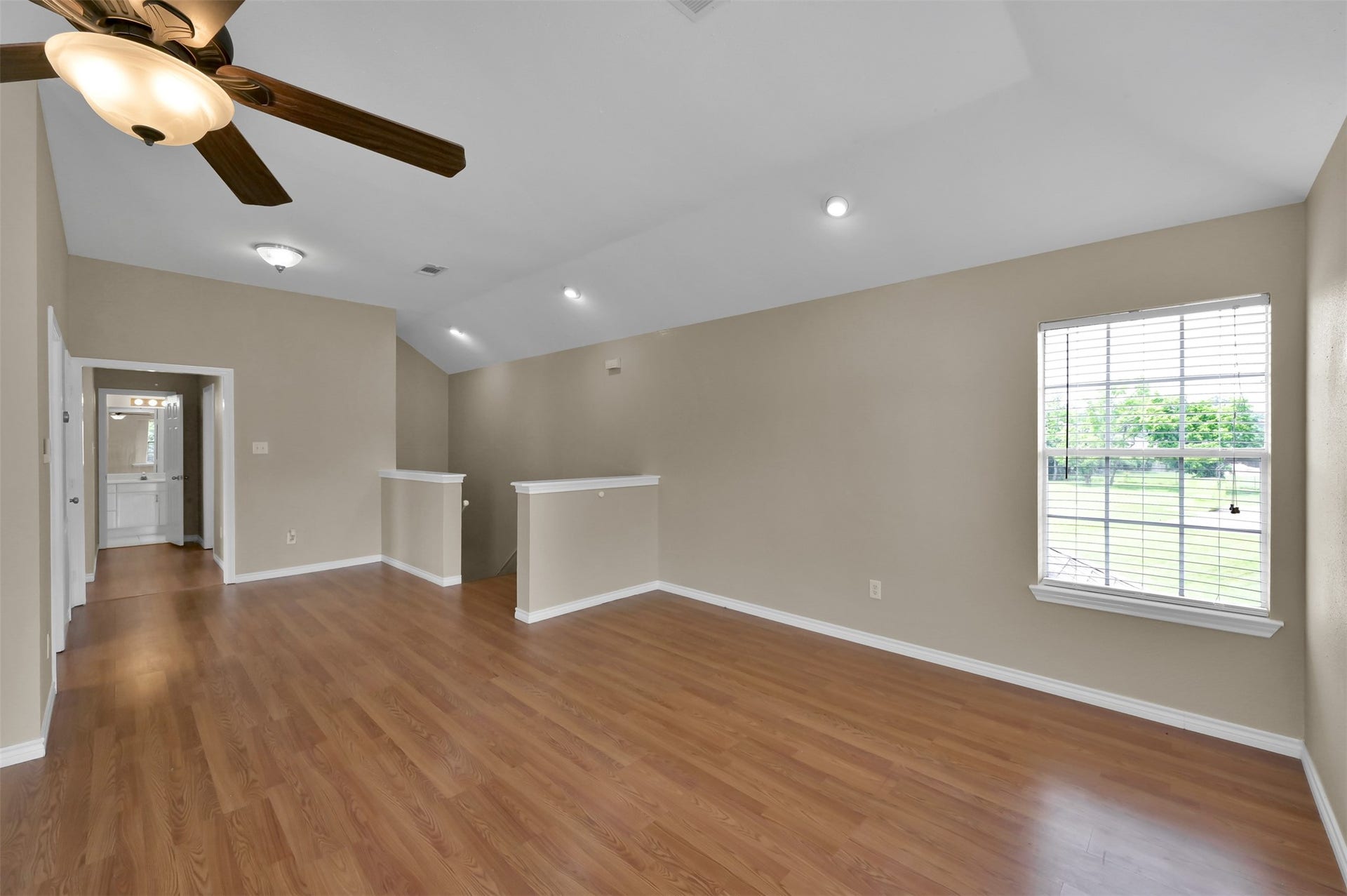1141 Lovett Street, Tomball, TX 77375 Bright, open room with warm wood flooring, a ceiling fan, and ample natural light from a large window, leading to additional living spaces.