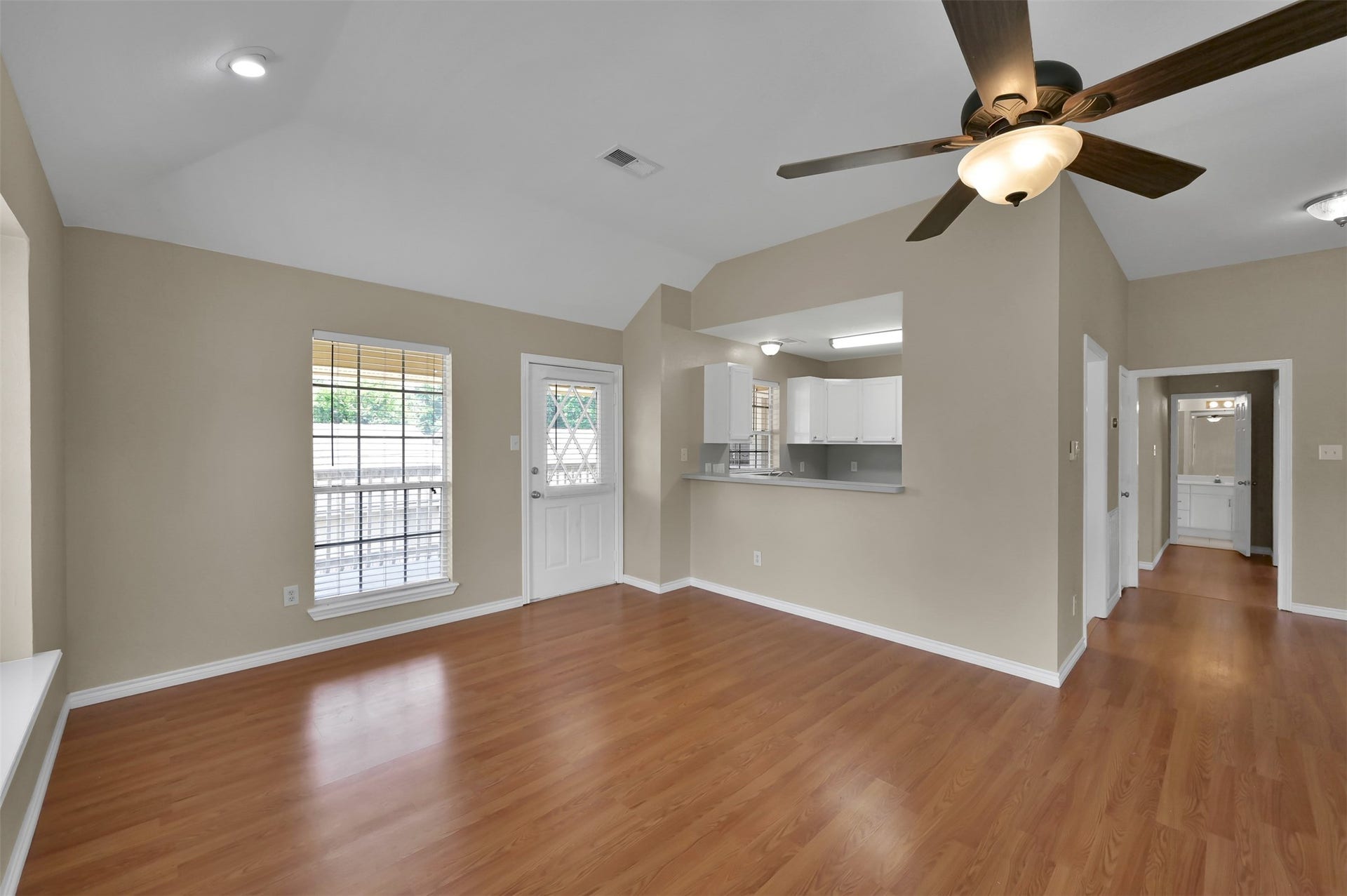 1141 Lovett Street, Tomball, TX 77375 Bright living area featuring sleek wood flooring, a vaulted ceiling with a modern fan, and an open-concept layout leading to the kitchen with a breakfast bar.