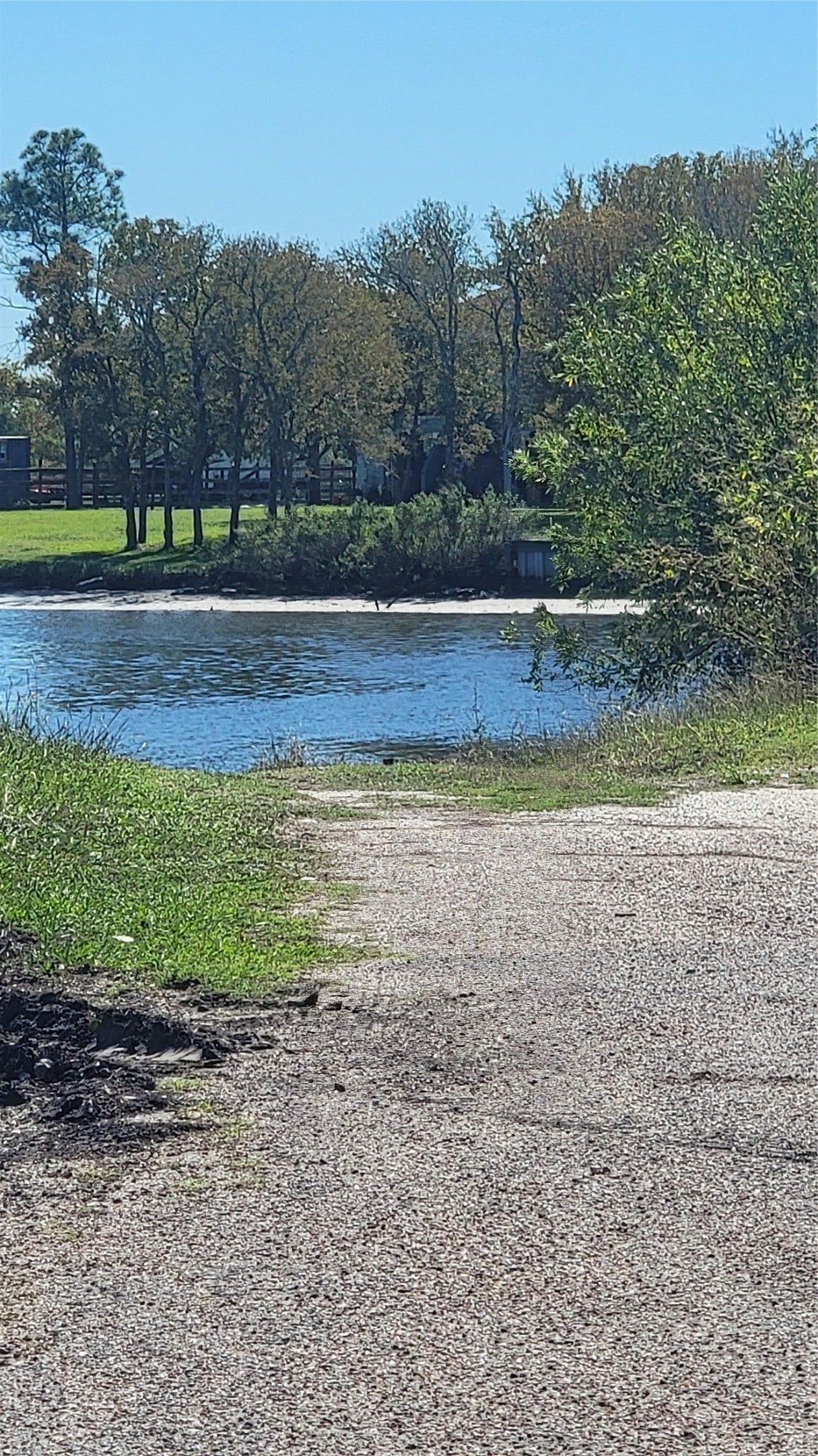 12018 Sandpiper Road, Angleton, TX 77515 This photo showcases a serene waterfront view with a paved path leading to a peaceful body of water, surrounded by lush greenery and trees, perfect for nature lovers.