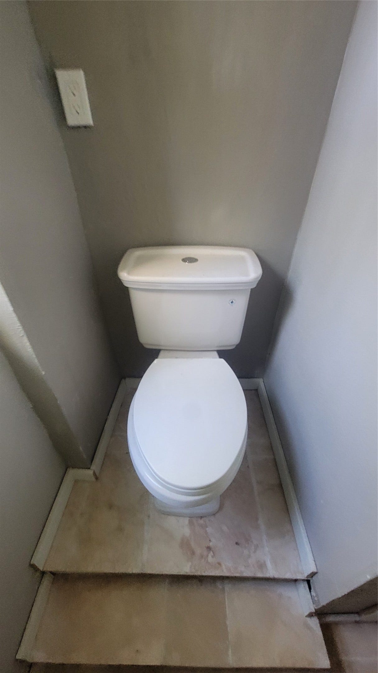12018 Sandpiper Road, Angleton, TX 77515 This photo shows a compact bathroom space featuring a white toilet placed on a small platform with tile flooring and gray walls.