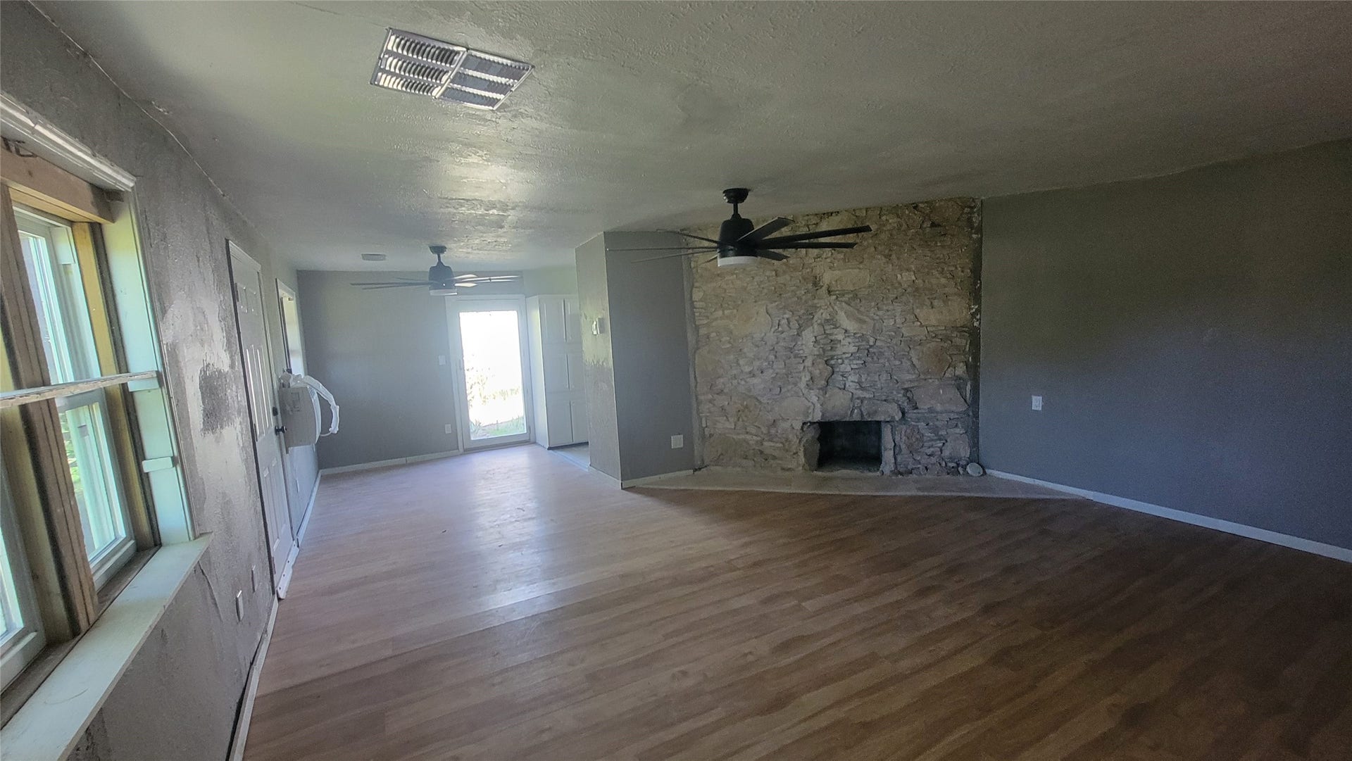 12018 Sandpiper Road, Angleton, TX 77515 This room features a rustic stone fireplace, two ceiling fans, and wood flooring. It has large windows for natural light and an open layout, offering a cozy and inviting atmosphere.