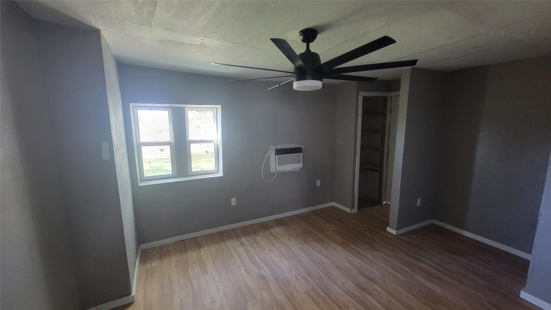 12018 Sandpiper Road, Angleton, TX 77515 This room features neutral-toned walls, a large ceiling fan, and a window for natural light. It includes an AC unit on the wall and a small closet area, with light wood flooring throughout.