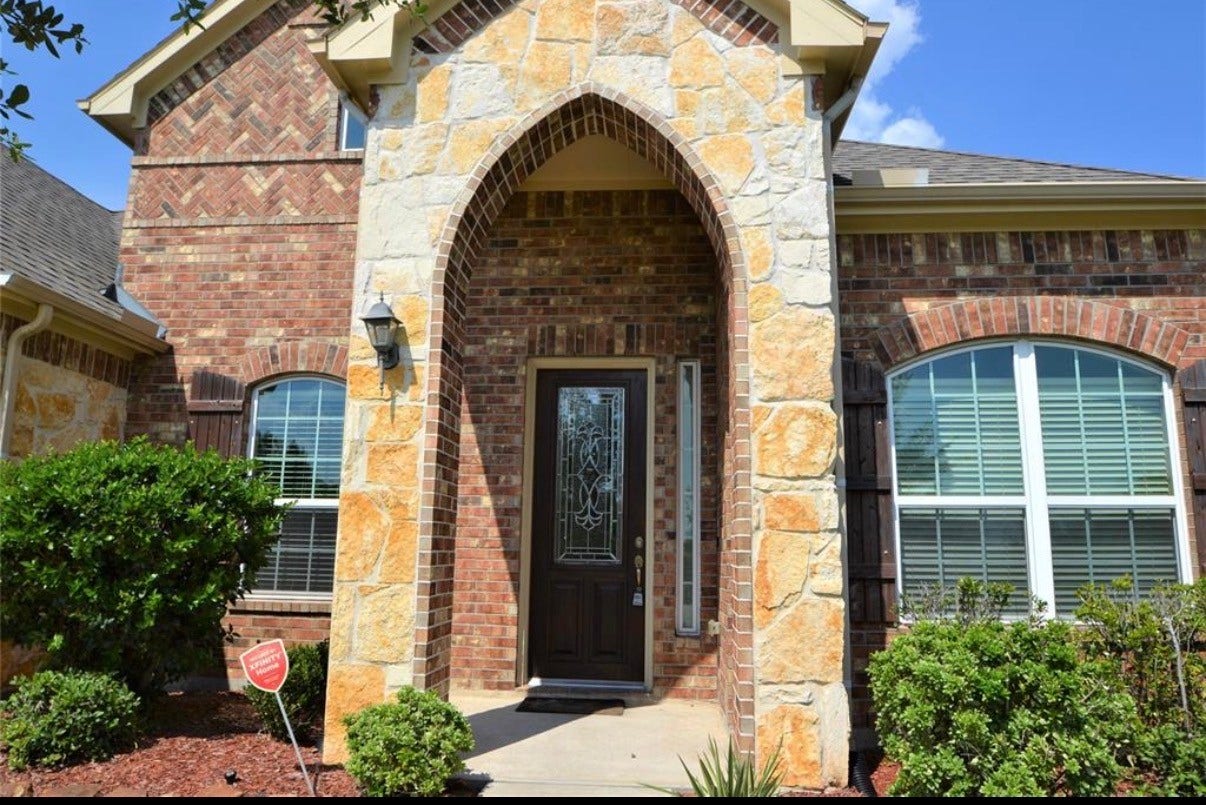Beautiful brick and stone faade with an elegant arched entryway, complemented by lush greenery and large windows for ample natural light.
