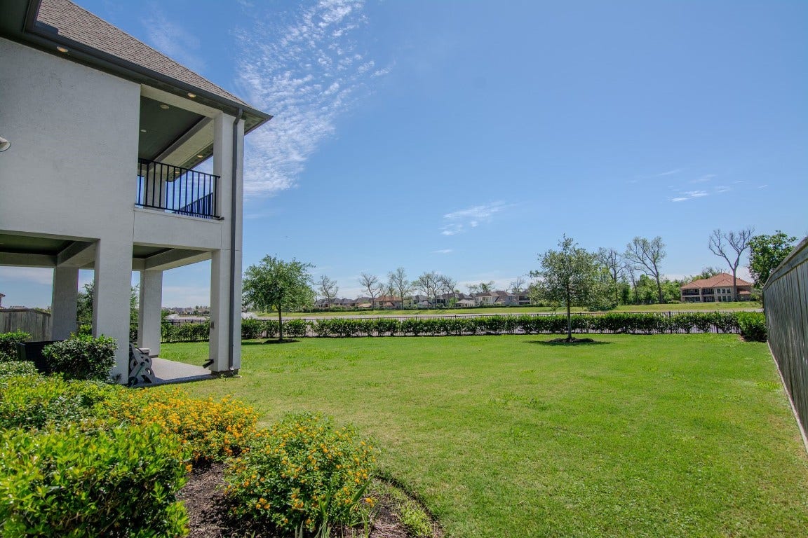5423 Priamus Drive, Missouri City, TX 77459 Spacious backyard with a well-maintained lawn, surrounded by a fence for privacy. The home features a covered patio and a balcony, perfect for outdoor relaxation. The area is bright and open, offering a serene view.