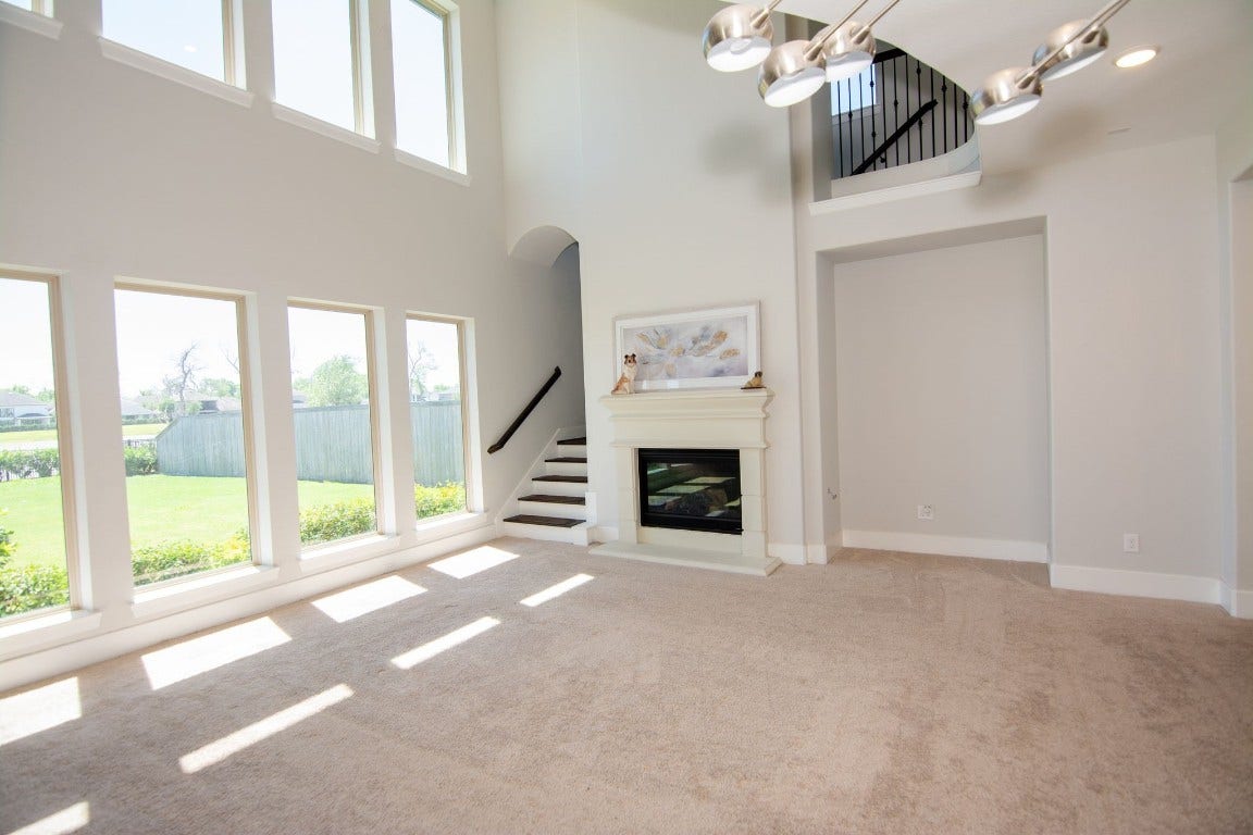 5423 Priamus Drive, Missouri City, TX 77459 This spacious living room features high ceilings, abundant natural light from large windows, a modern fireplace, and a sleek staircase leading to an upper level. The neutral tones and open layout enhance the airy feel.