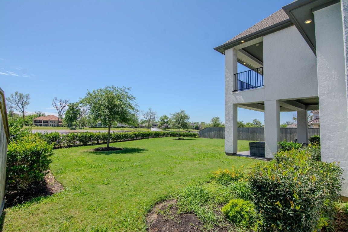 5423 Priamus Drive, Missouri City, TX 77459 This photo features a spacious backyard with a well-maintained lawn and some shrubbery, adjacent to a two-story home with a covered patio. The area is fenced, providing privacy, and there's a view of neighboring houses and trees, offering a serene and open atmosphere.