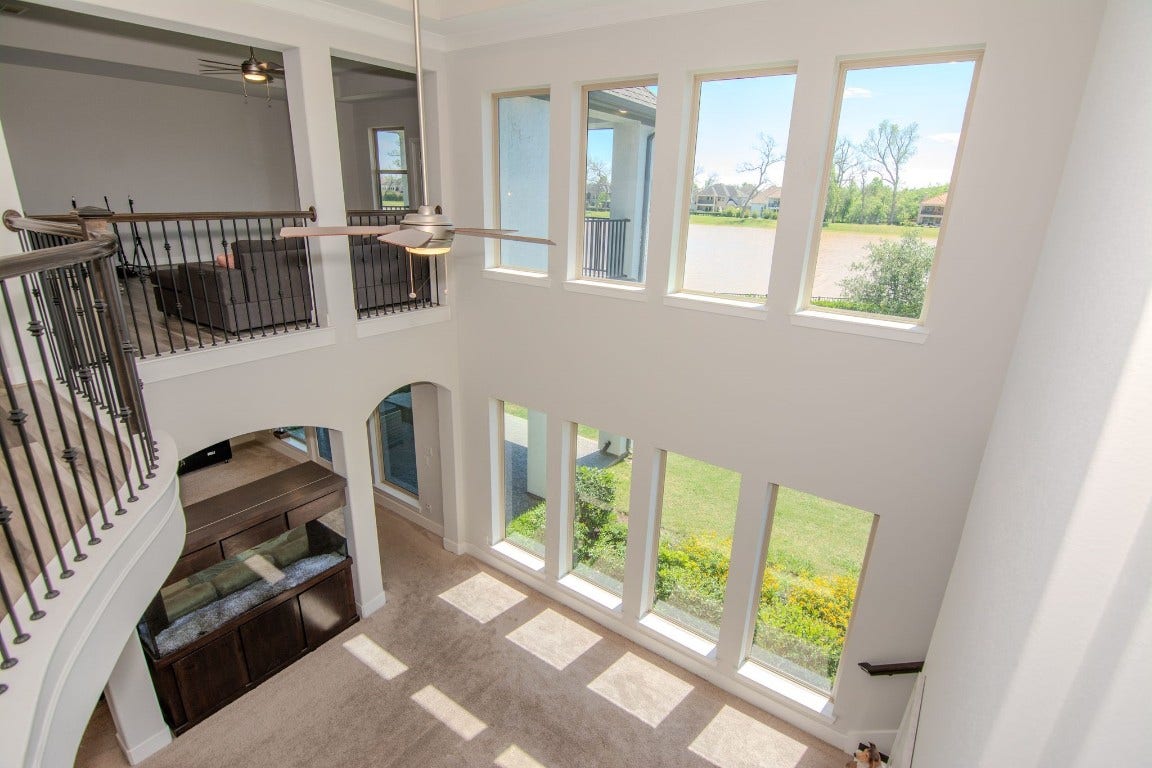 5423 Priamus Drive, Missouri City, TX 77459 This spacious home features a bright, open living area with high ceilings and large windows offering scenic views of the outdoors. The upper-level railing overlooks the room, enhancing the open feel.