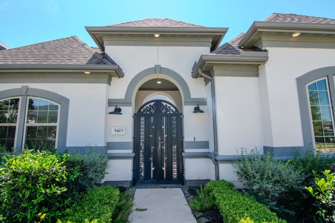 5423 Priamus Drive, Missouri City, TX 77459 This photo showcases an elegant, modern home exterior with a stylish arched entrance, ornate front door, and well-maintained landscaping. The facade features a neutral color palette with gray accents, enhancing its curb appeal.