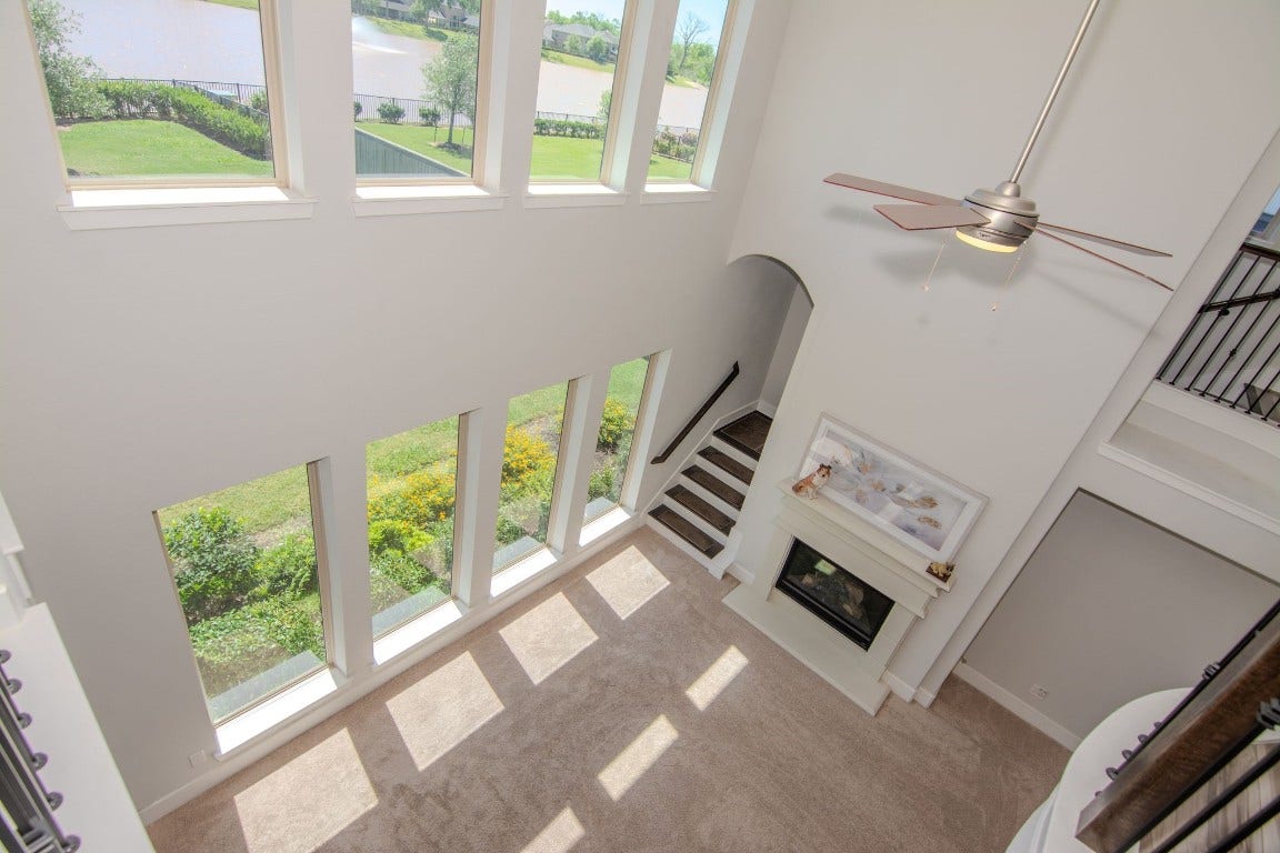 5423 Priamus Drive, Missouri City, TX 77459 This spacious living area features a high ceiling and expansive windows that offer abundant natural light and scenic views. It includes a modern ceiling fan and a stylish fireplace, creating a cozy yet airy atmosphere.