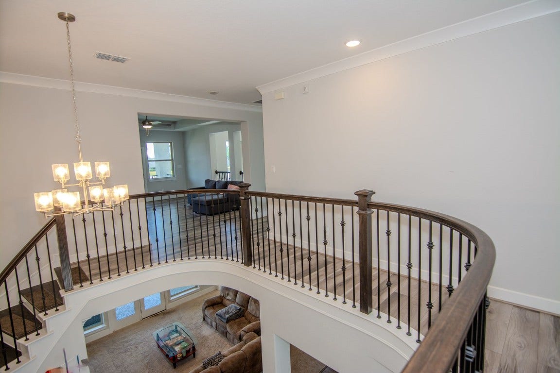 5423 Priamus Drive, Missouri City, TX 77459 This photo showcases a modern home interior with an elegant curved staircase and iron railings. The open floor plan features a view into a spacious living area with natural light. A stylish chandelier adds a touch of sophistication.