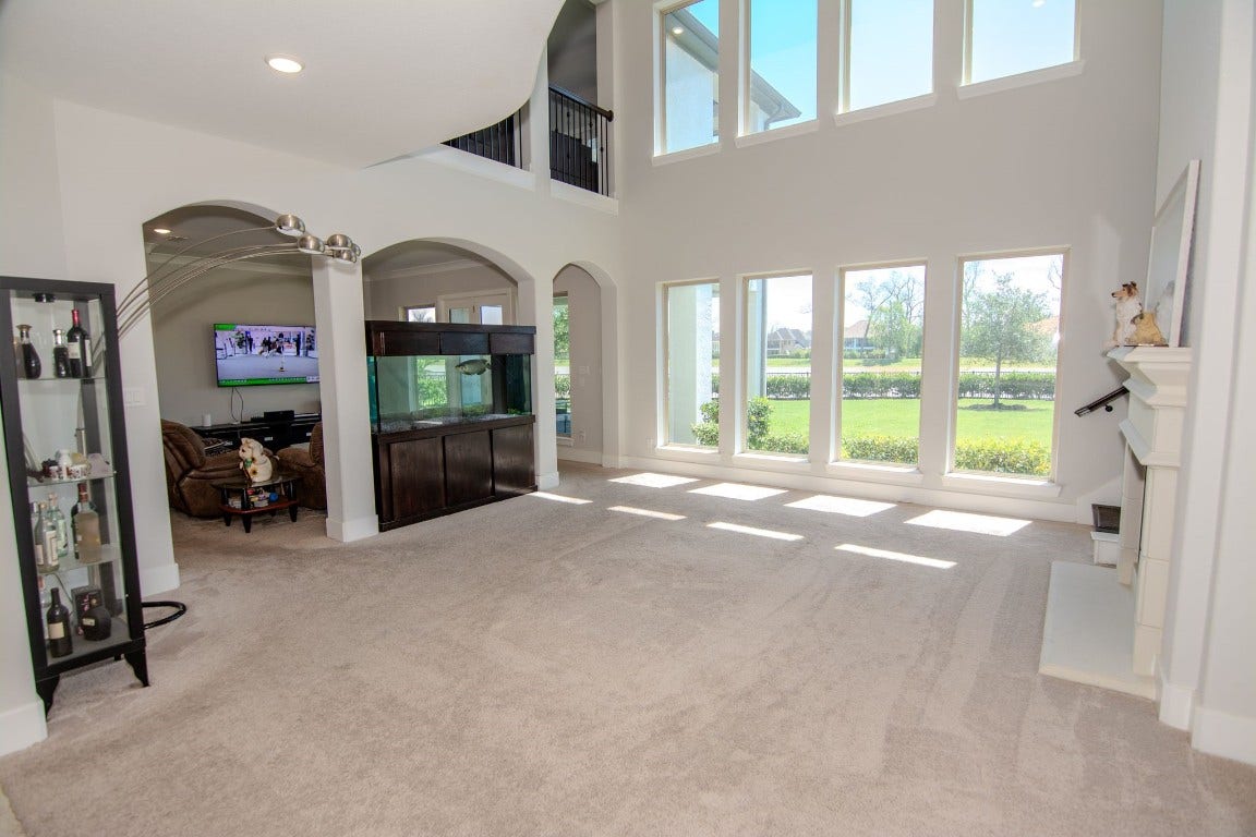 5423 Priamus Drive, Missouri City, TX 77459 This spacious living area features high ceilings and large windows, offering abundant natural light and a scenic view. It includes a cozy seating area, modern decor, and a built-in aquarium, providing a perfect blend of comfort and elegance.