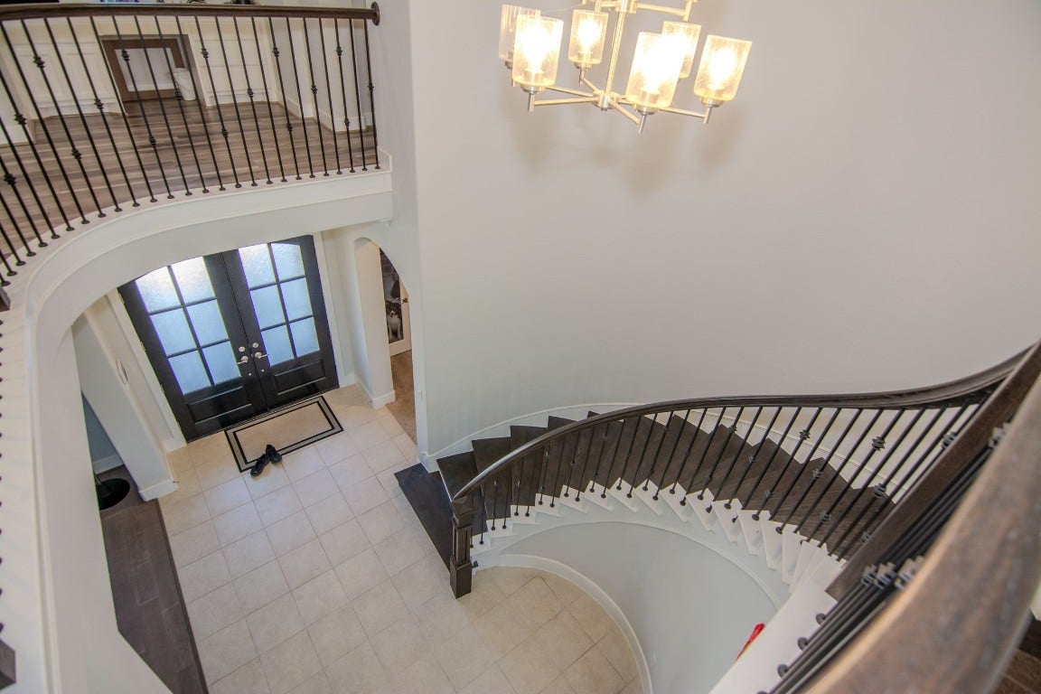 5423 Priamus Drive, Missouri City, TX 77459 This photo showcases a bright and open foyer with a stunning spiral staircase, elegant tile flooring, and a modern chandelier. The double front doors feature glass panels, enhancing the welcoming atmosphere.