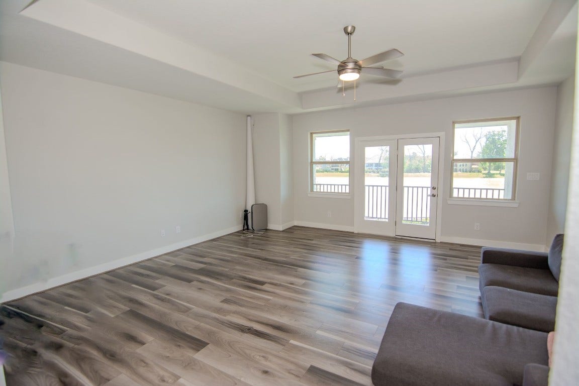 5423 Priamus Drive, Missouri City, TX 77459 This spacious living room features modern wood flooring, neutral walls, and large windows that let in plenty of natural light. A ceiling fan adds comfort, and glass doors open to a scenic outdoor view, enhancing the airy, open feel.
