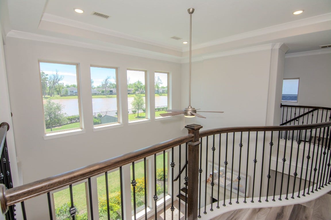 5423 Priamus Drive, Missouri City, TX 77459 This photo showcases a spacious, bright upper landing with large windows offering scenic water views. It features elegant railing and a modern ceiling fan, enhancing the airy, open feel.