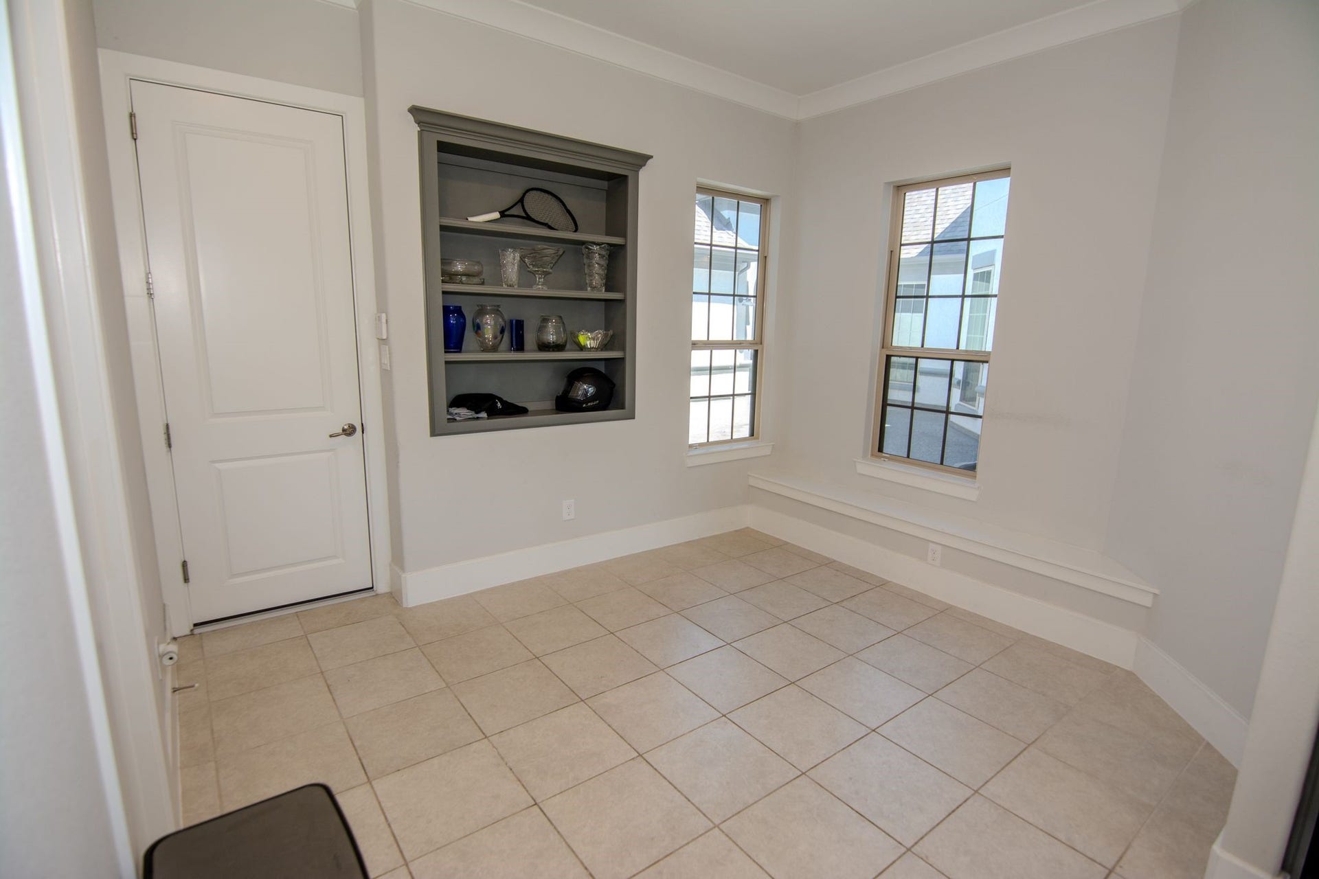 5423 Priamus Drive, Missouri City, TX 77459 This room features neutral tile flooring, built-in wall shelving, and two large windows that let in plenty of natural light. There's a white door for entry and a ledge beneath the windows, offering additional seating or display space.