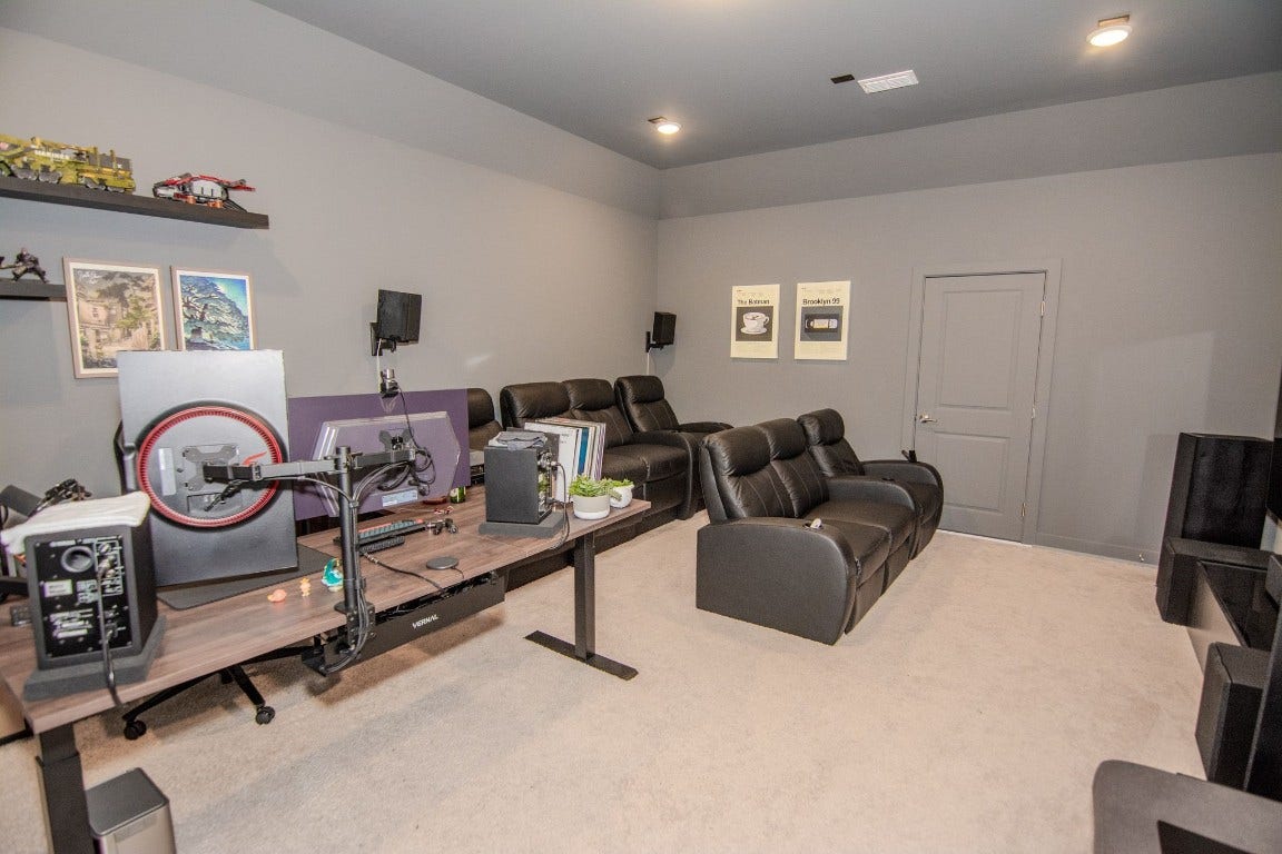 5423 Priamus Drive, Missouri City, TX 77459 This photo showcases a cozy home theater room featuring plush leather recliners and a large desk setup. The walls are painted in a neutral tone, complemented by soft carpeting. Wall-mounted speakers and framed art contribute to the inviting atmosphere, making it an ideal space for entertainment and work.