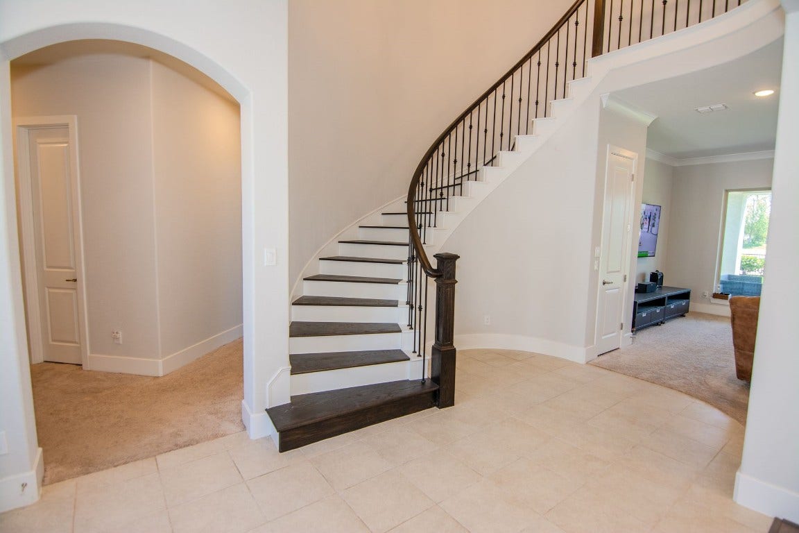 5423 Priamus Drive, Missouri City, TX 77459 This photo showcases a bright entryway with a striking curved staircase featuring dark wood steps and elegant iron railings. The open layout leads to a cozy living area, and the neutral tones create a welcoming atmosphere.