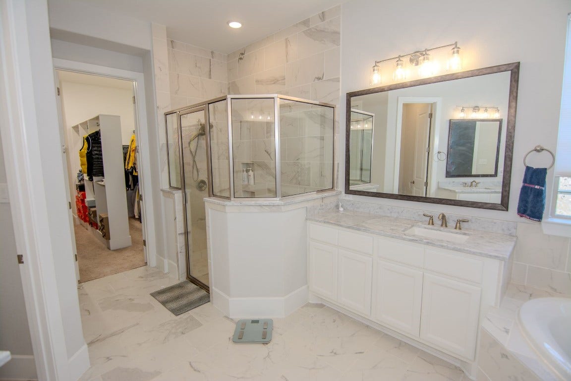 5423 Priamus Drive, Missouri City, TX 77459 This bright, modern bathroom features a spacious glass-enclosed shower, elegant marble countertops, and ample cabinet space. A large mirror and stylish lighting enhance the room, while an adjacent walk-in closet offers convenient storage.