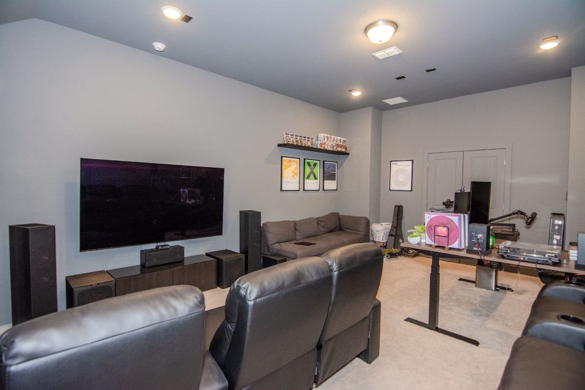 5423 Priamus Drive, Missouri City, TX 77459 This photo showcases a modern home theater room with comfortable leather seating, a large wall-mounted TV, surround sound speakers, and a cozy sofa. The room has a sleek, minimalist design with gray walls, recessed lighting, and decorative artwork.