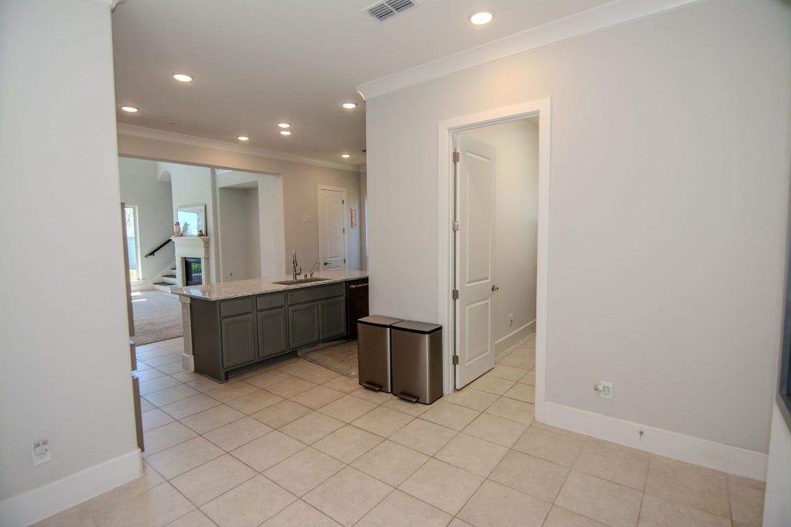 5423 Priamus Drive, Missouri City, TX 77459 This photo showcases a modern, open-concept interior with neutral tile flooring and recessed lighting. The space includes a kitchen area with a sleek island, and visible access to a cozy living room with a fireplace.
