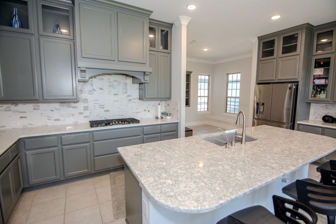 5423 Priamus Drive, Missouri City, TX 77459 This kitchen features sleek gray cabinetry with ample storage, a spacious marble countertop island with a sink, and modern stainless steel appliances, creating a stylish and functional space.