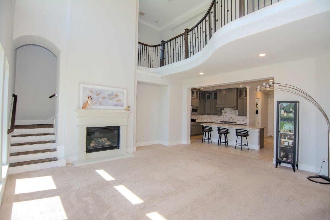 5423 Priamus Drive, Missouri City, TX 77459 This spacious living area features high ceilings, abundant natural light, and an open layout. It includes a cozy fireplace, a modern kitchen with bar seating, and a curved staircase, creating a welcoming and elegant atmosphere.