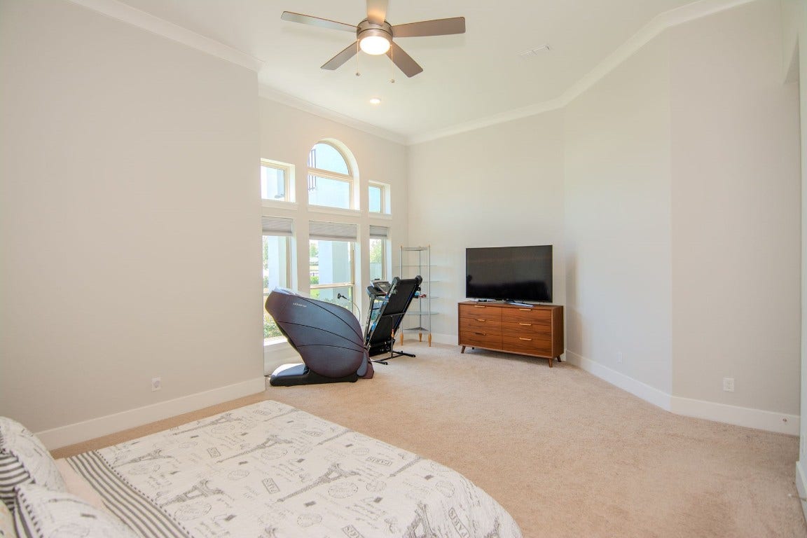 5423 Priamus Drive, Missouri City, TX 77459 This spacious primary bedroom features high ceilings, a ceiling fan, and large arched windows that provide ample natural light. The room includes a cozy seating area.