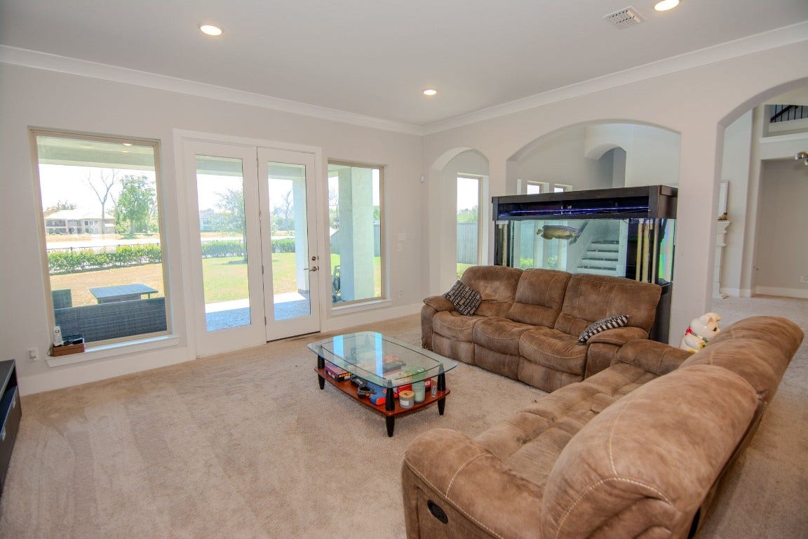 5423 Priamus Drive, Missouri City, TX 77459 This spacious living room features plush carpeting, a large fish tank, and ample natural light from multiple windows and glass doors leading to a patio. Perfect for relaxation and entertaining.