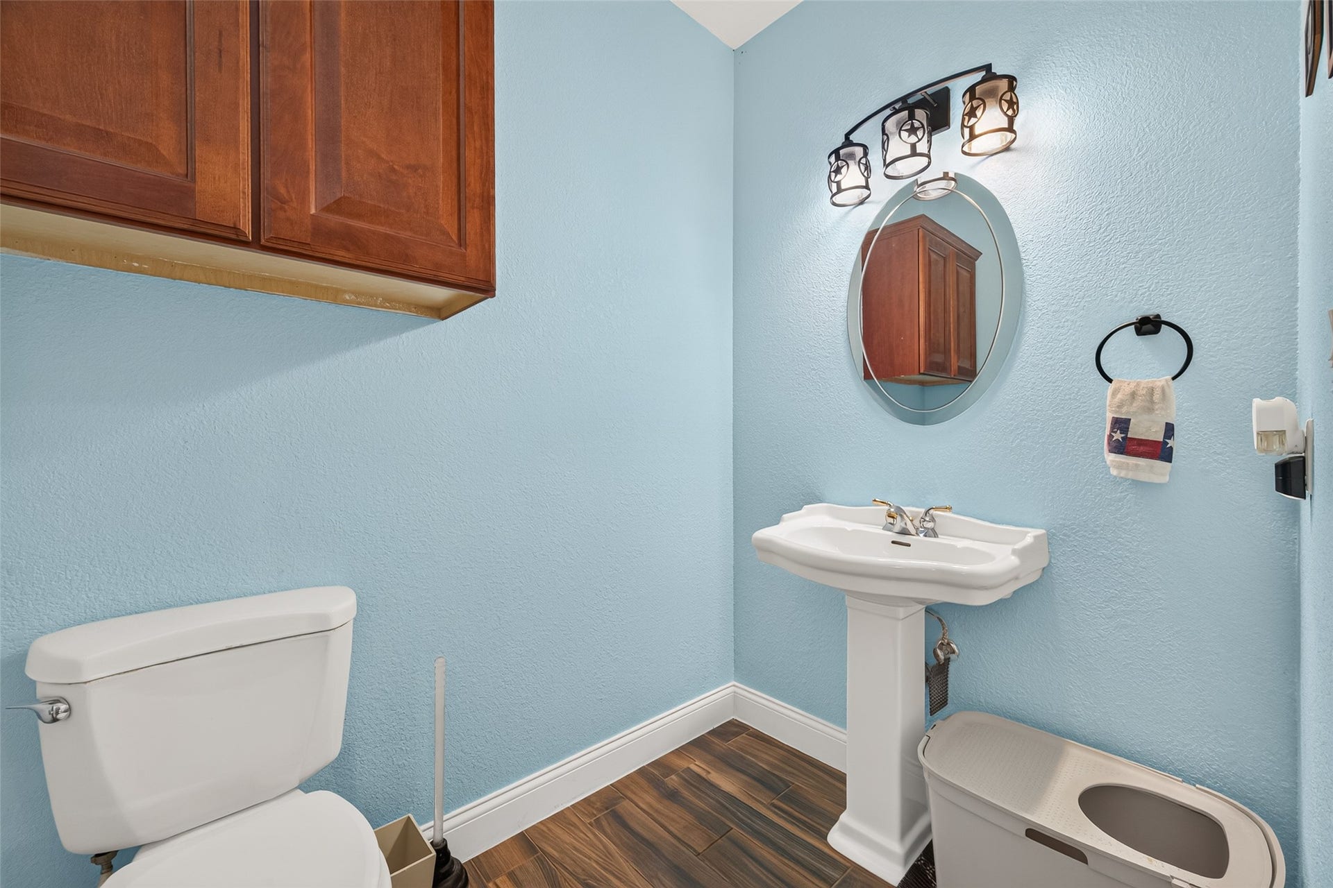 Conveniently located near the laundry room and garage, this half bath features a pedestal sink, decorative lighting, additional cabinet storage, and beautiful wood-look flooring.