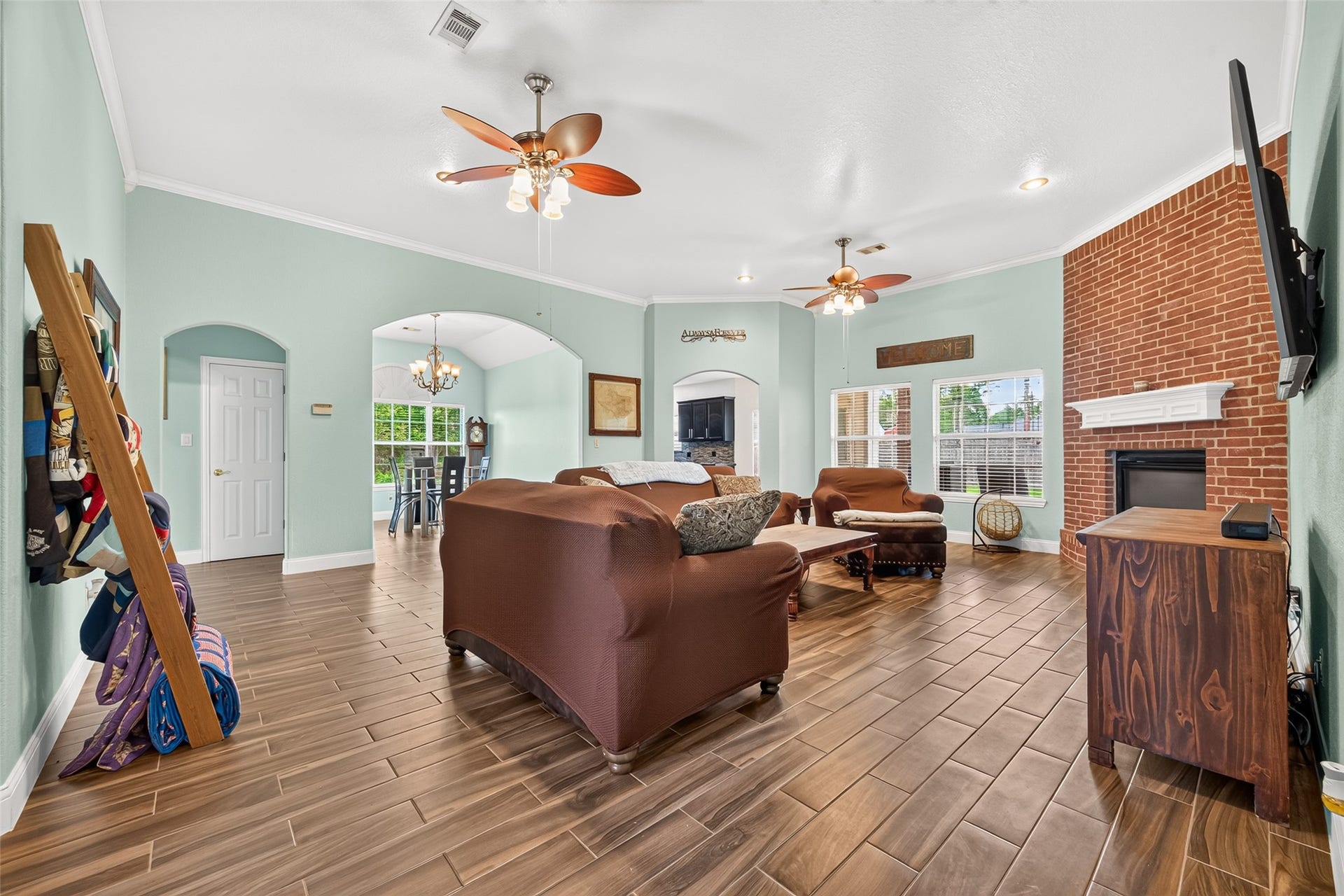Impressive living area featuring high ceilings, beautiful wood-look flooring, a corner brick fireplace, and plenty of room to relax or entertain!