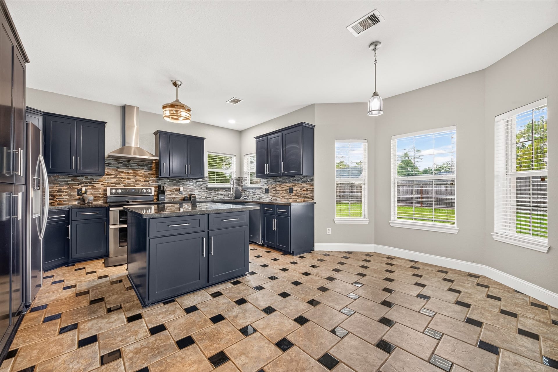 Spacious kitchen featuring rich dark cabinetry, a center island, stainless steel appliances, and a bright breakfast area surrounded by windows.