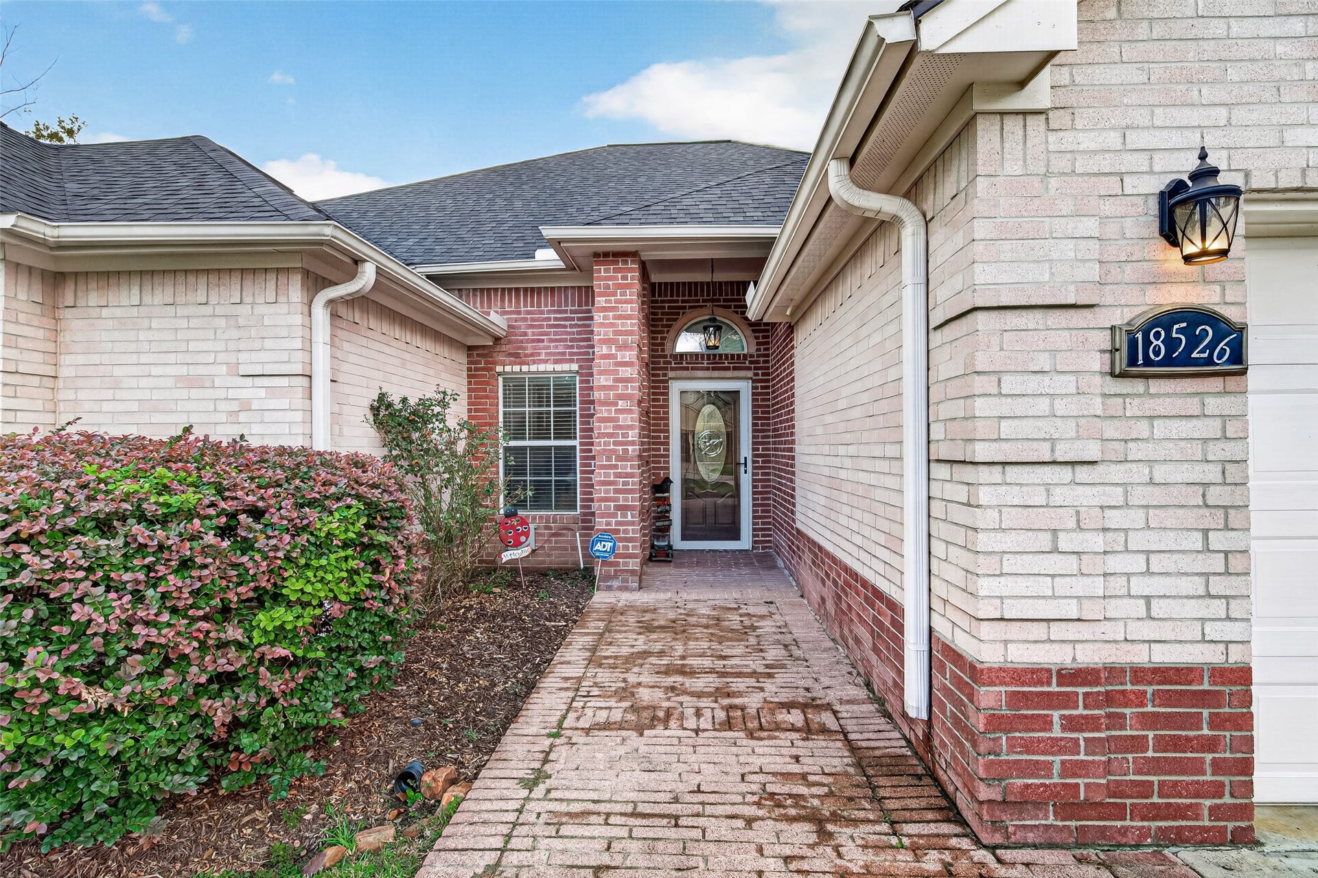 A warm welcome begins here! Charming brick entryway with beautiful landscaping, a brick-paver walkway, and an inviting covered front entrance.