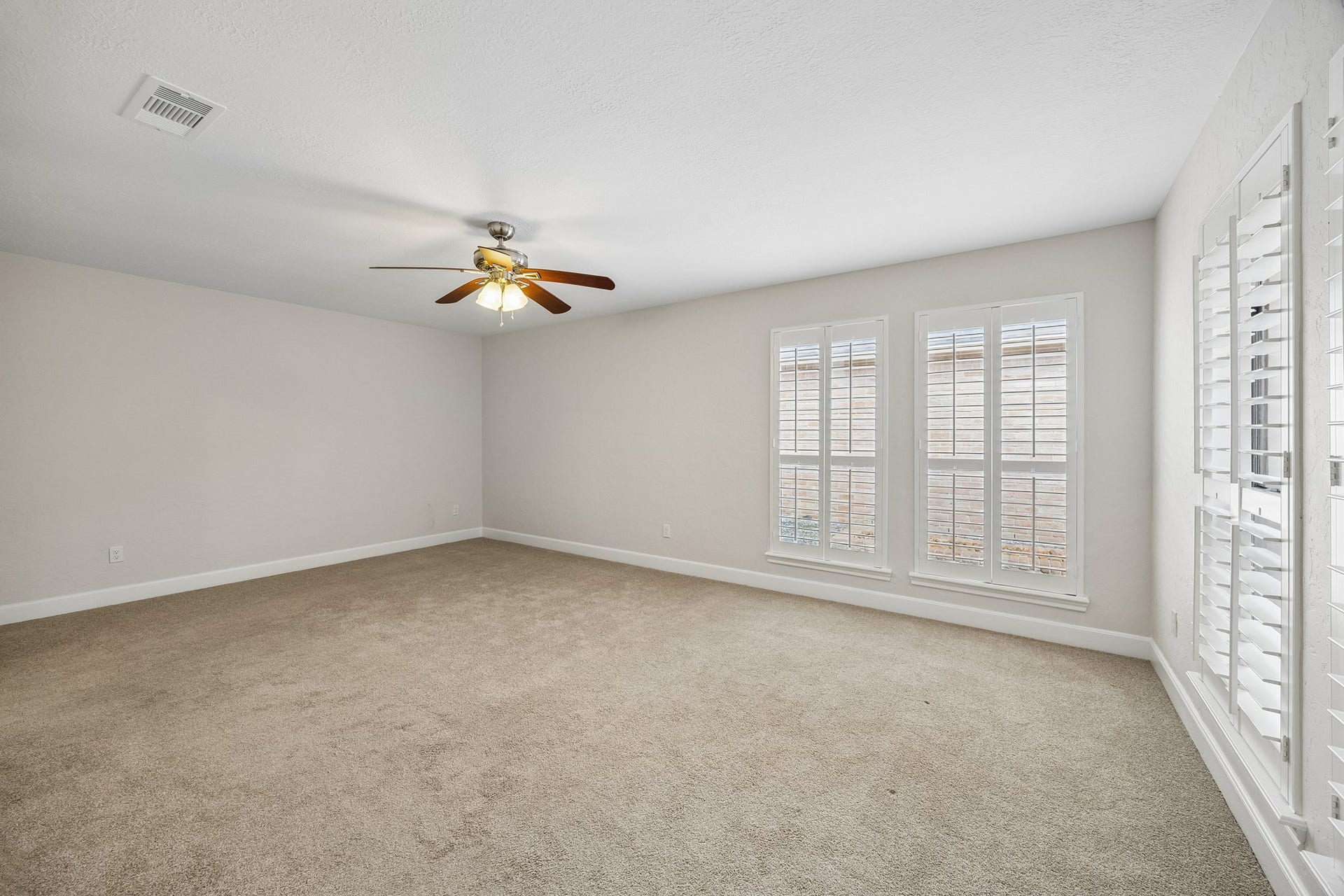 Primary bedroom with ceiling fan and plantation shutters. This room overlooks the covered back patio.