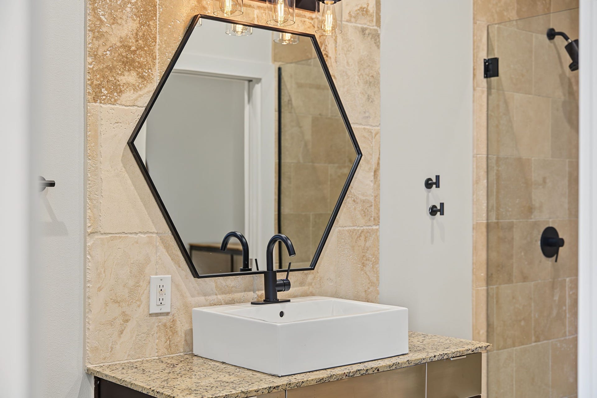 A Touch of Modern Sophistication! A striking vessel sink sits atop the beautiful granite countertop, creating a stylish focal point in this contemporary bathroom. A framed hexagon mirror and sleek over-sink lighting complete the look, adding a polished designer touch to the space!