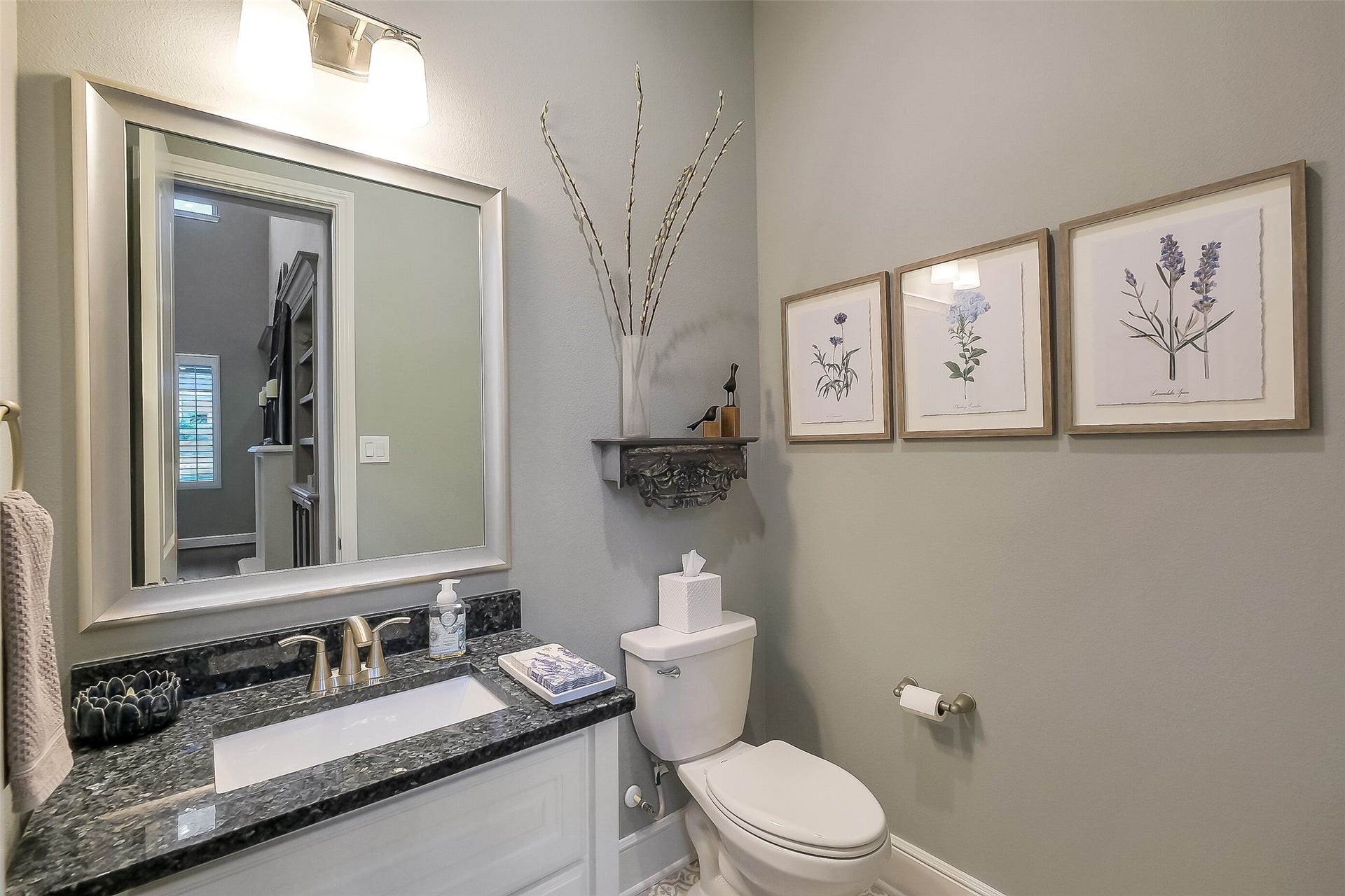 The first floor powder bathroom features granite counters, framed mirror and trending floor tile