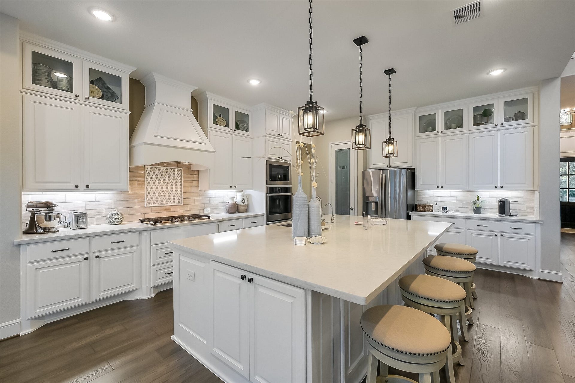 This bright white kitchen is built for both everyday living and entertaining, with a large quartz island, designer pendant lighting, and glass-front cabinetry that extends to the ceiling. The walk in pantry and storage under the island ensure you have storage for all of your cooking and