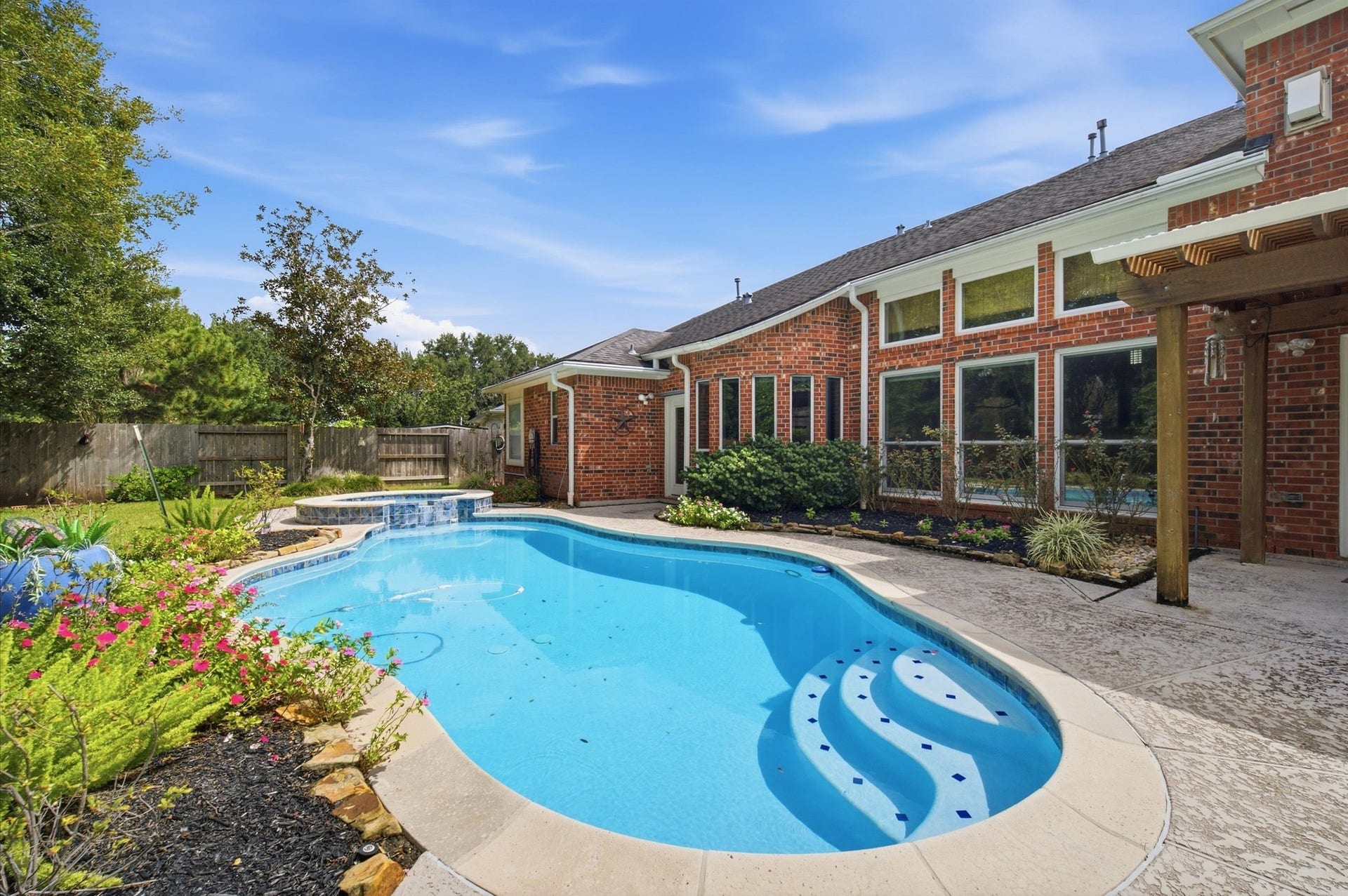 4427 Shady River, Missouri City, TX 77459 Stunning backyard oasis featuring a sparkling pool with elegant curved lines, surrounded by lush landscaping and a charming brick exterior.