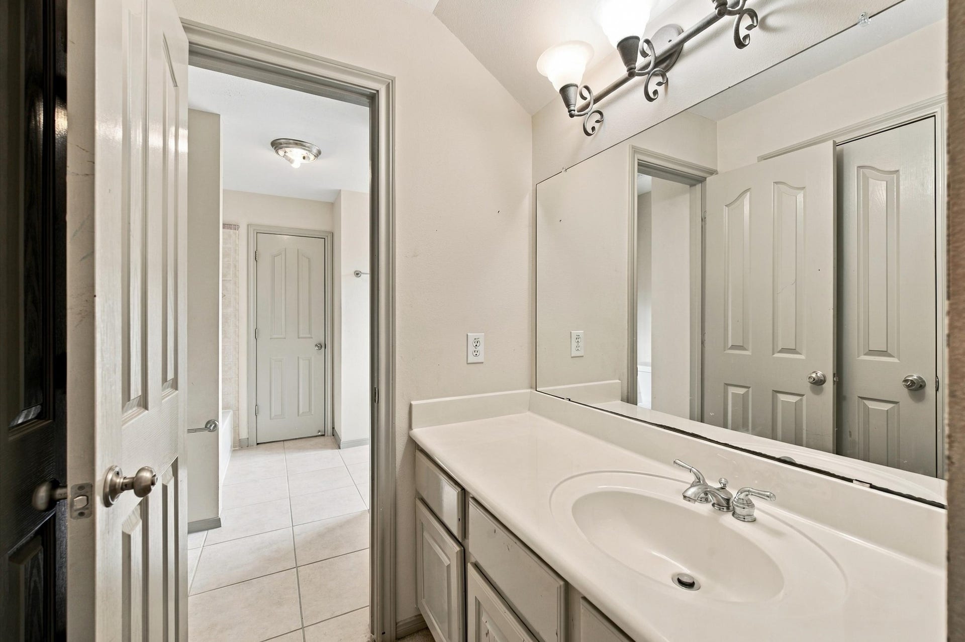 4427 Shady River, Missouri City, TX 77459 Bright bathroom featuring a large mirror, elegant lighting, and ample counter space, leading to a tiled hallway.